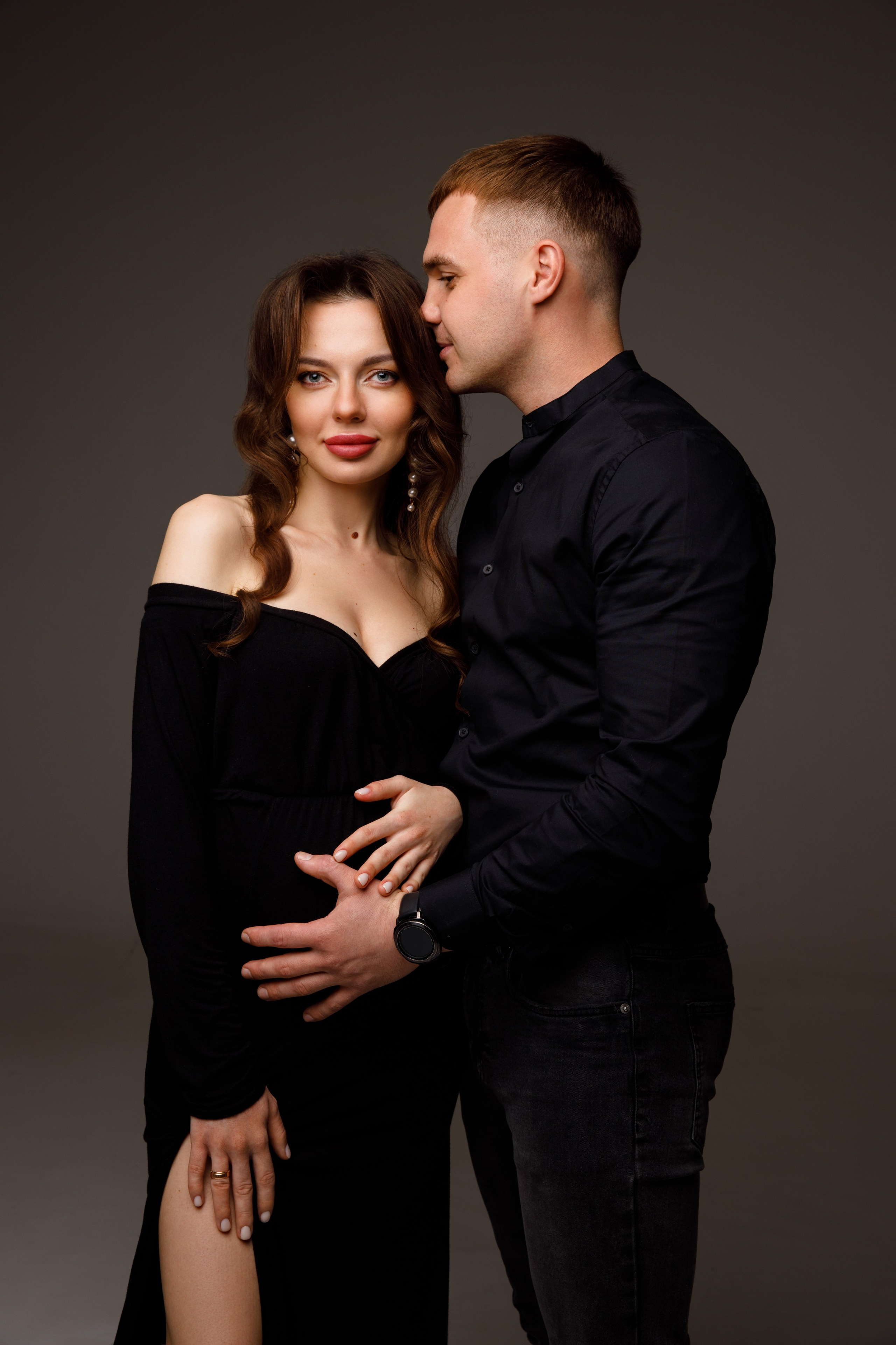 Беременная фотосессия с мужем в черных образах на сером фоне.