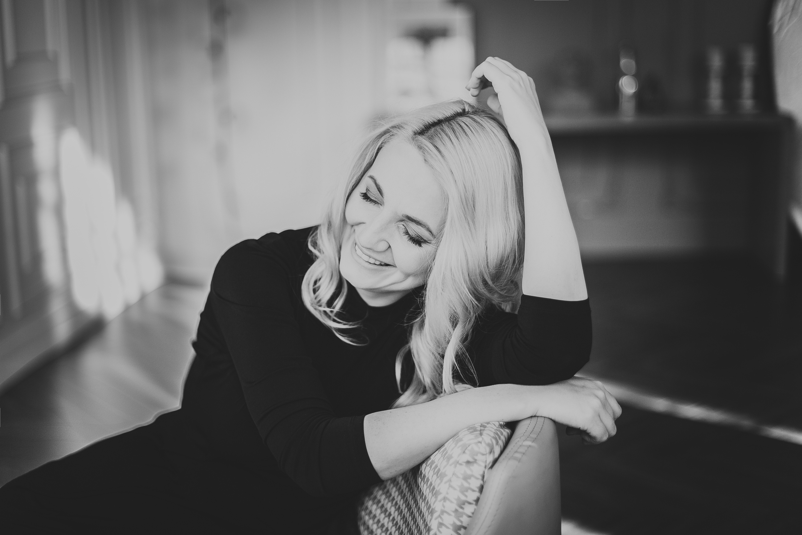 блондинка смеется опершись на спинку кресла