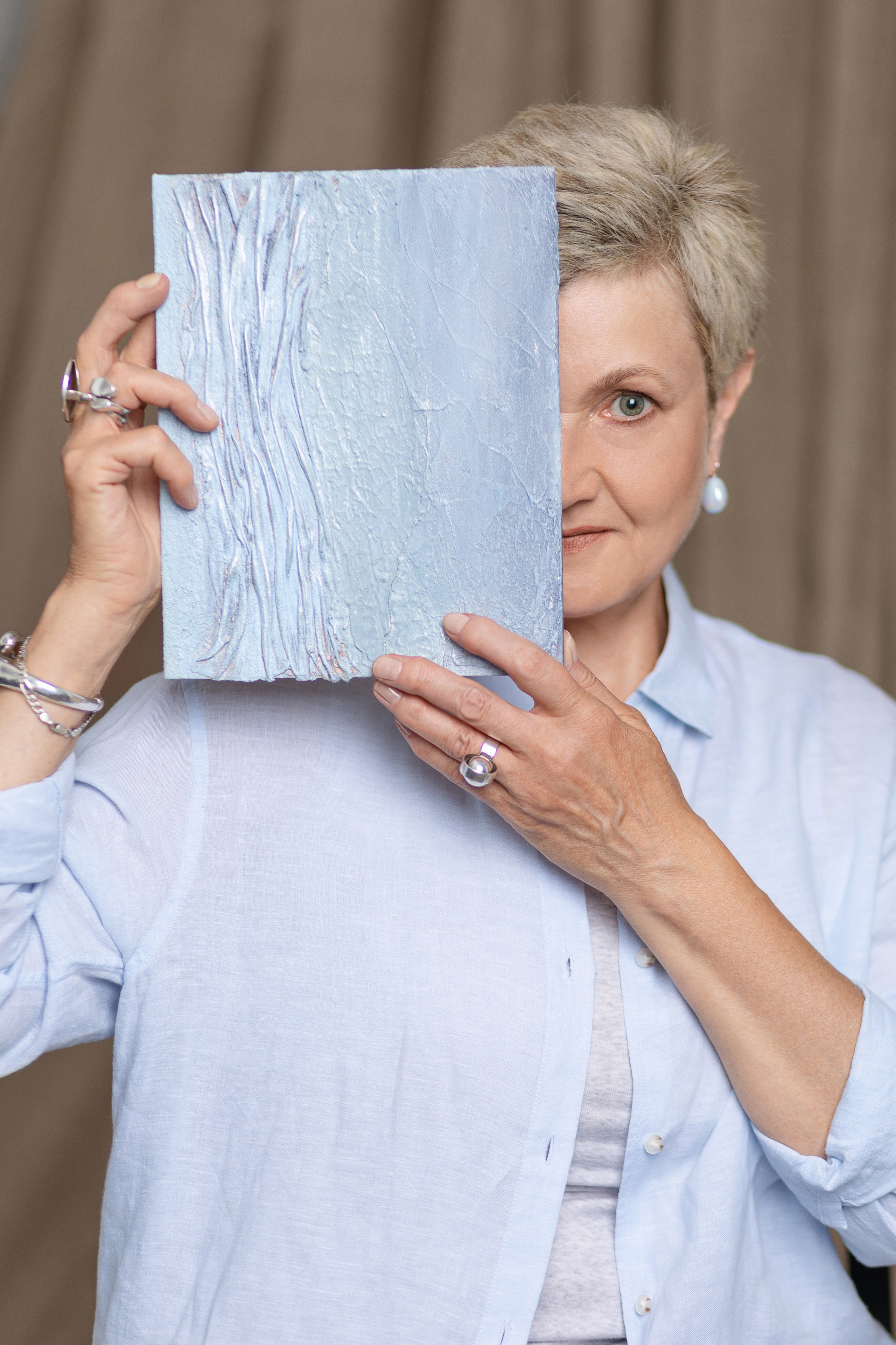 Художница держит высоко свою картину, закрывающую половину лица художницы.