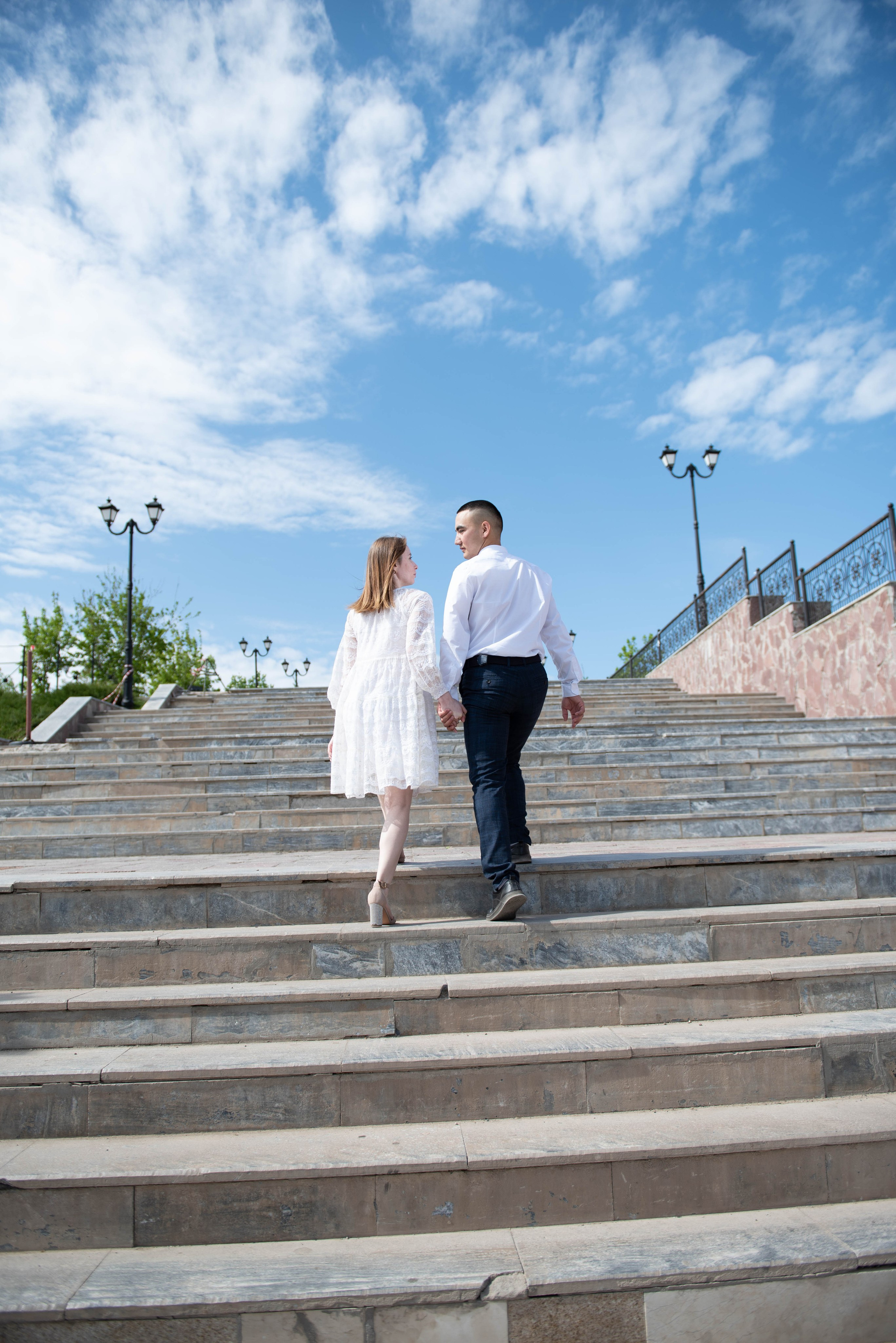 Свадебная фотосессия летом на улице. Влюбленная пара идет по ступенькам вверх по лестнице.