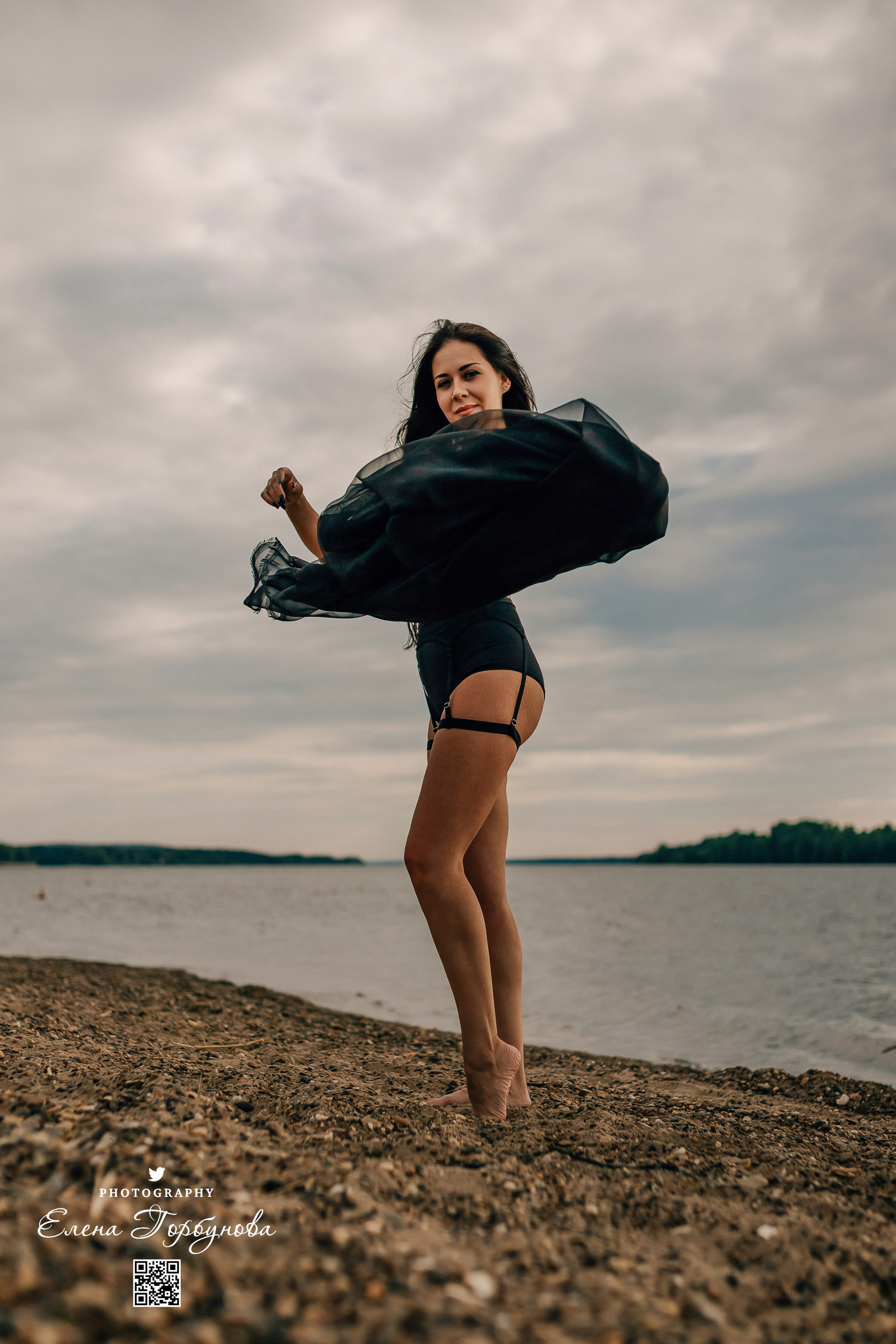 Фотосессия с черной тканью. Легкая черная вуаль летит на вертру. Фотосессия у реки черная серия с тканью. Девушка укуталась в черную ткань. Прогулка по набережной. Песок, речка, модель в черном. Качели над водой, Закат. Девушка лежит на песке. В зеленых деревьях