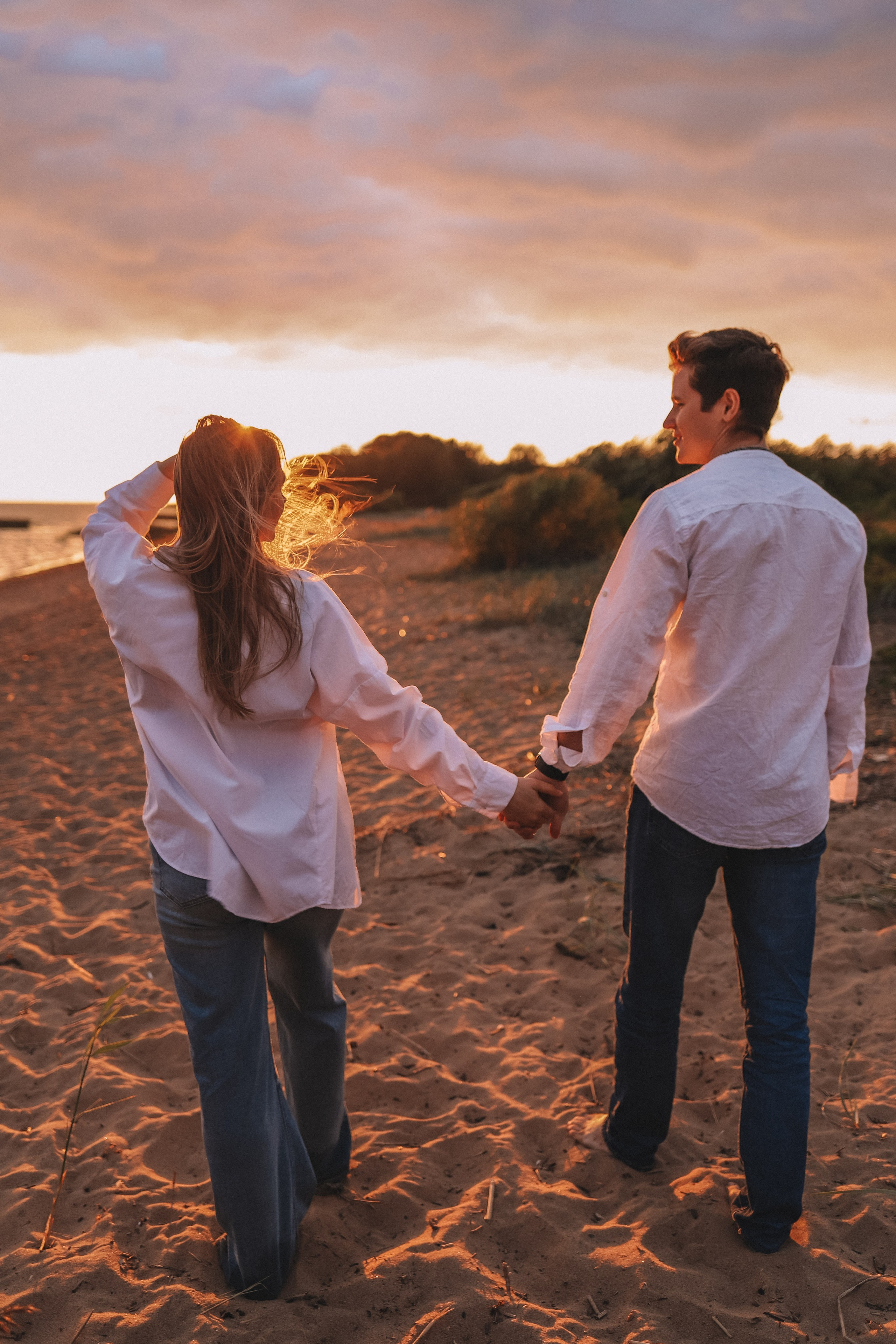 Пара держится за руки, наблюдают закат