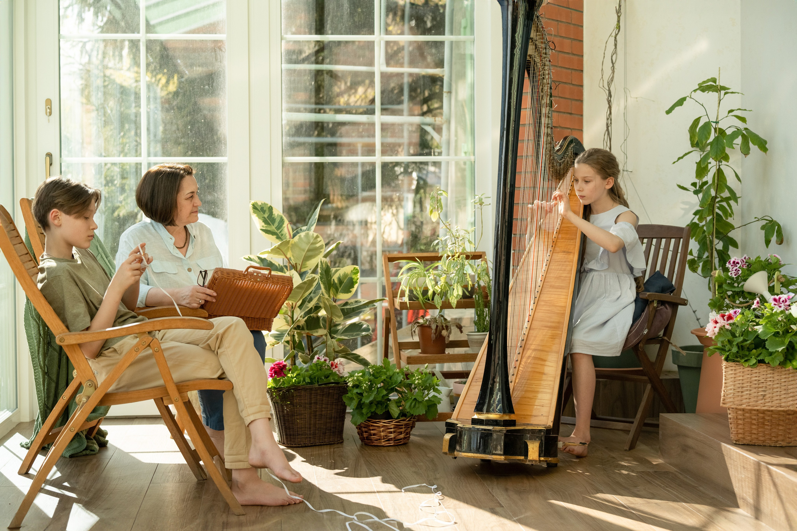 Девочка играет на арфе, а бабушка с братом слушают ее музыку.