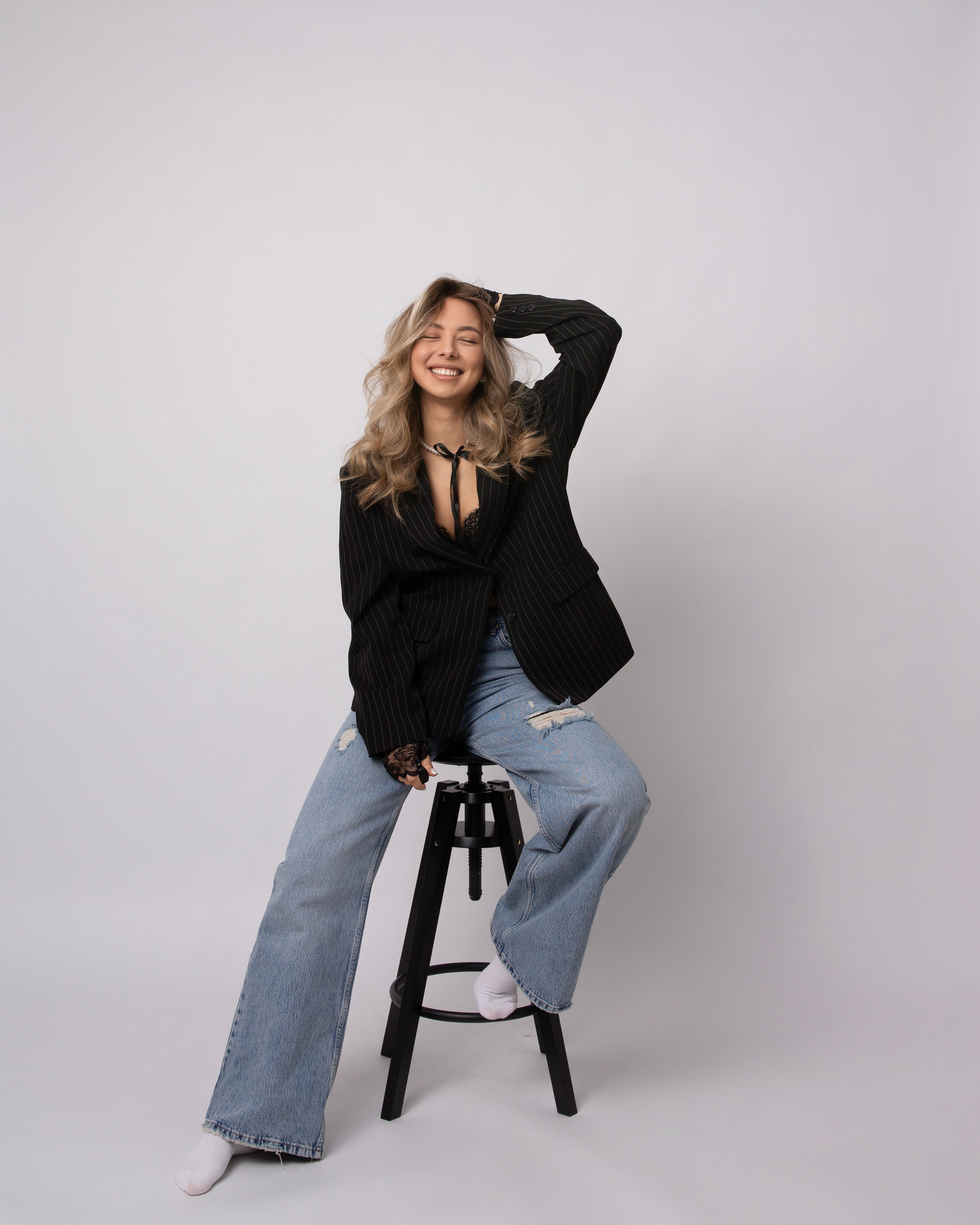 Автопортрет улыбающейся блондинки на барном стуле позирует на белом фоне в фотостудии Fotomaris