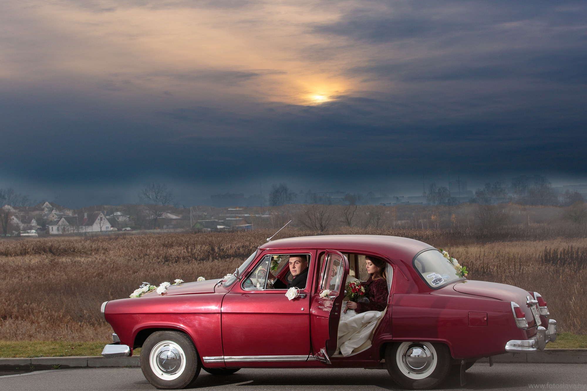 жених с невестой в ретро автомобиле на фоне красивого неба.