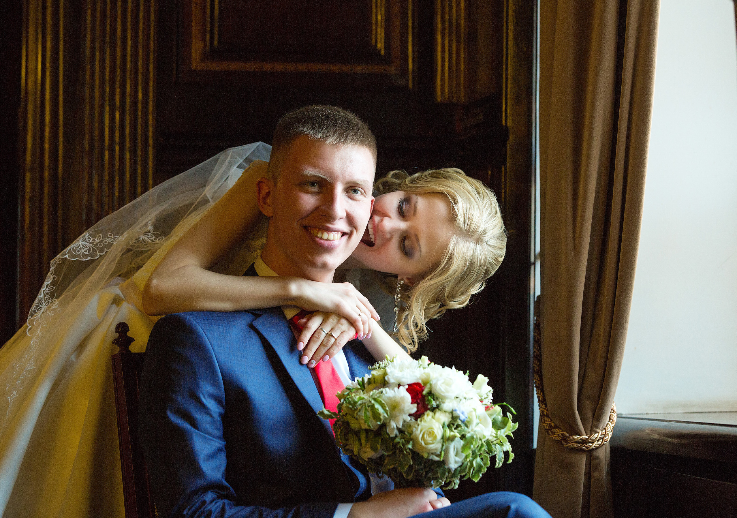 жених сидит,невеста обнимает его сзади и целует в щеку.