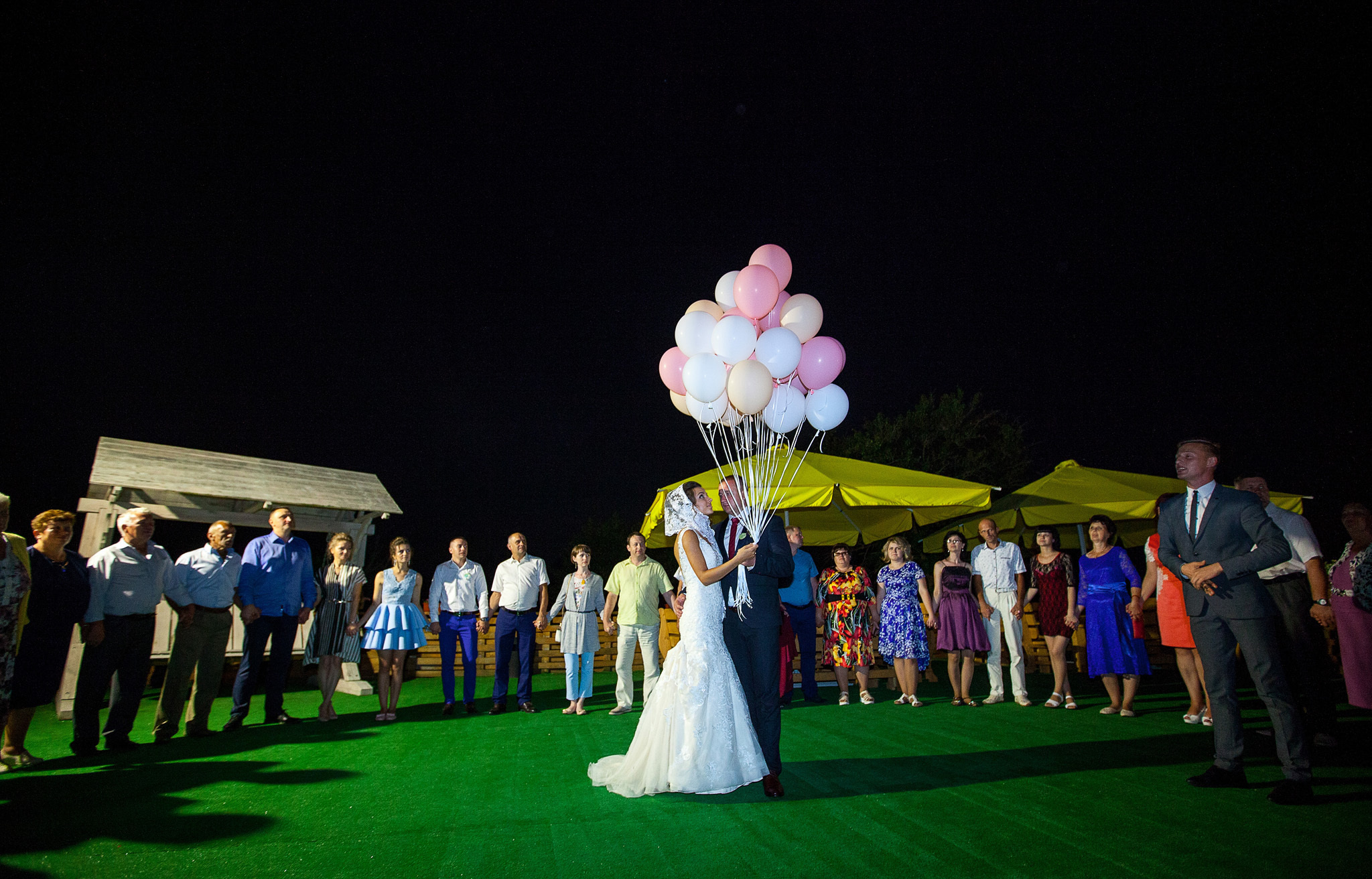 жених с невестой на фоне гостей запускают воздушные шарики.