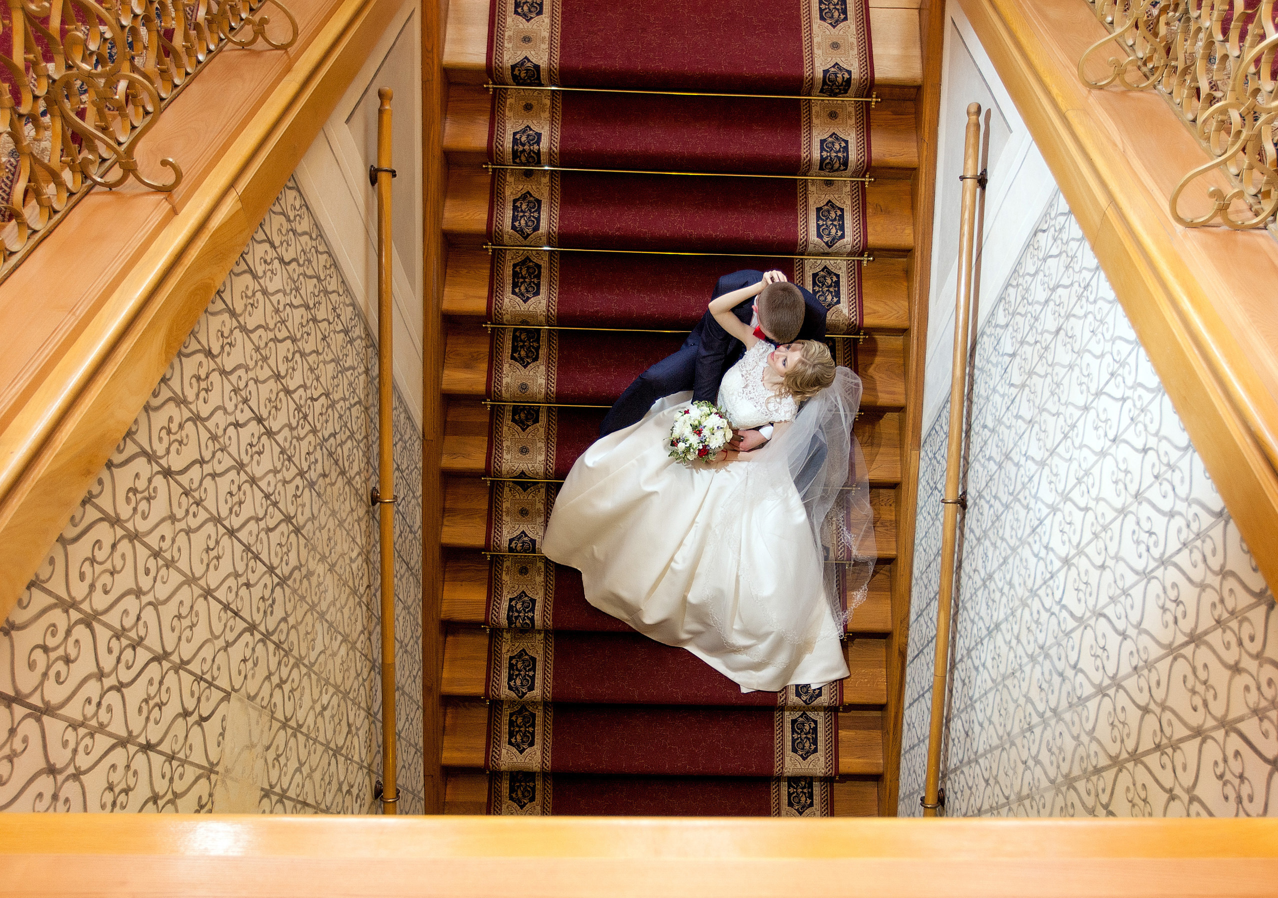 фото сверху, жених с невестой сидят на лестнице с красной дорожкой.