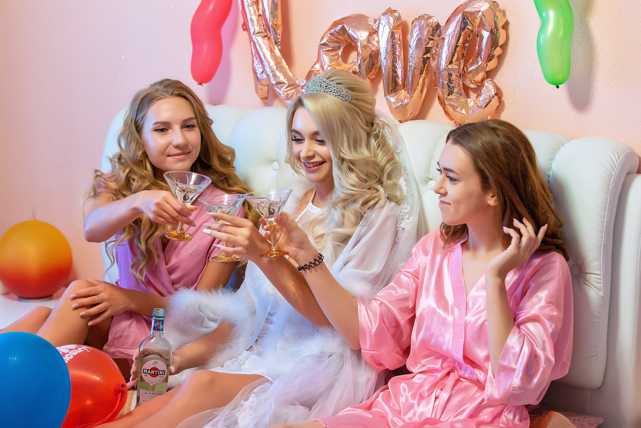 невеста с подружками с шампанским в руках весело сидят на кровати.