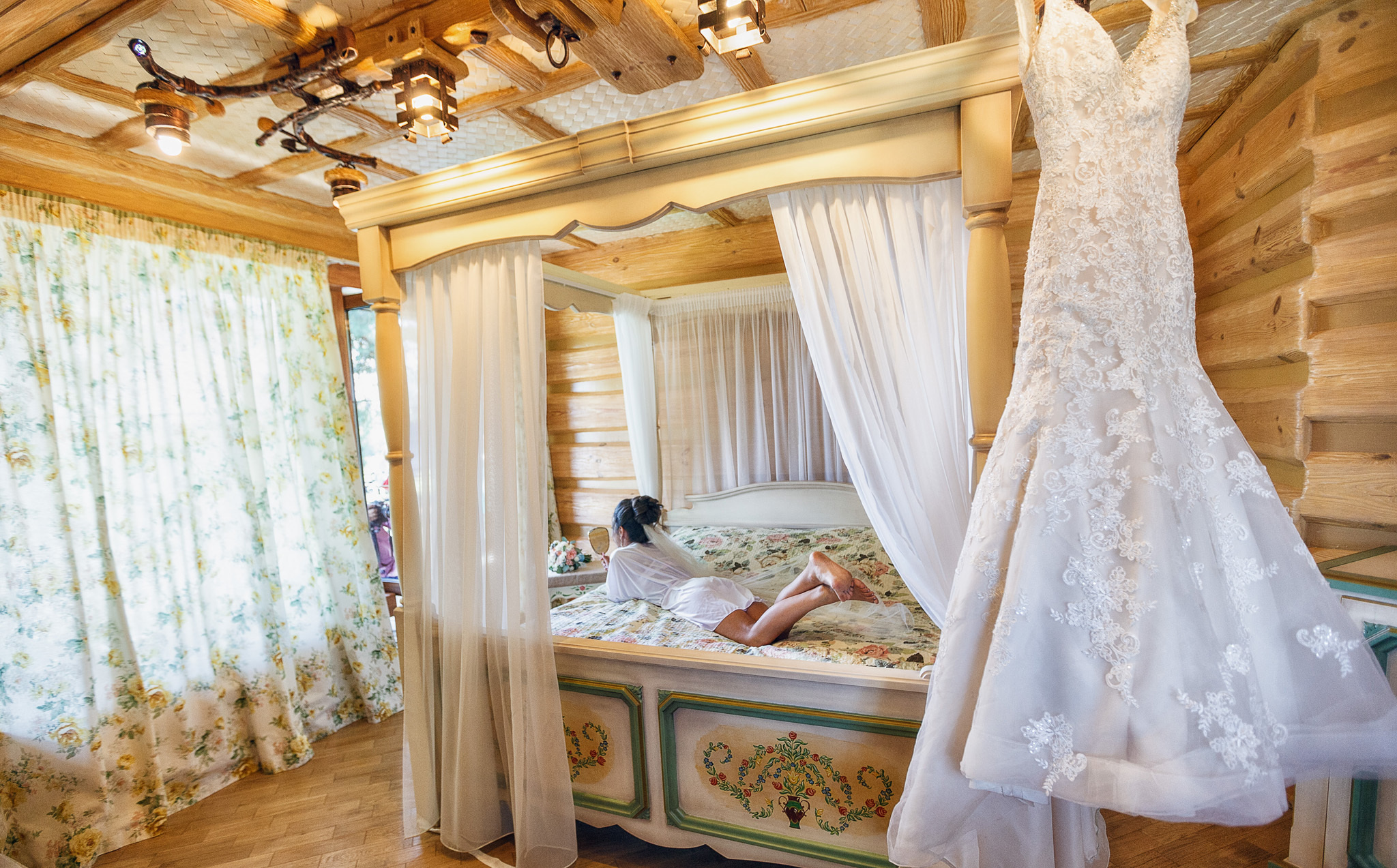 невеста в пеньюаре лежит на брачном ложе на фоне свадебного платья.
