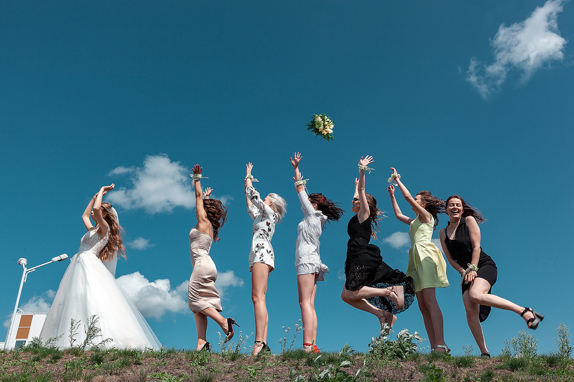 подружки невесты на фоне синего неба ловят букет невесты.