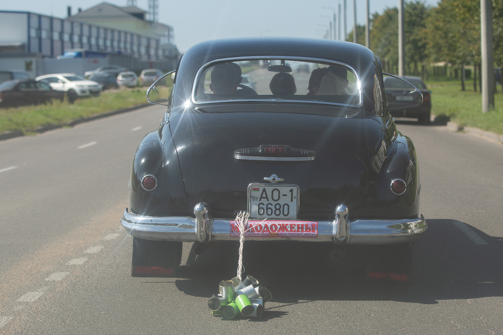 свадебный ретро автомобиль с консервными банками на веревке в движении, вид  сзади.