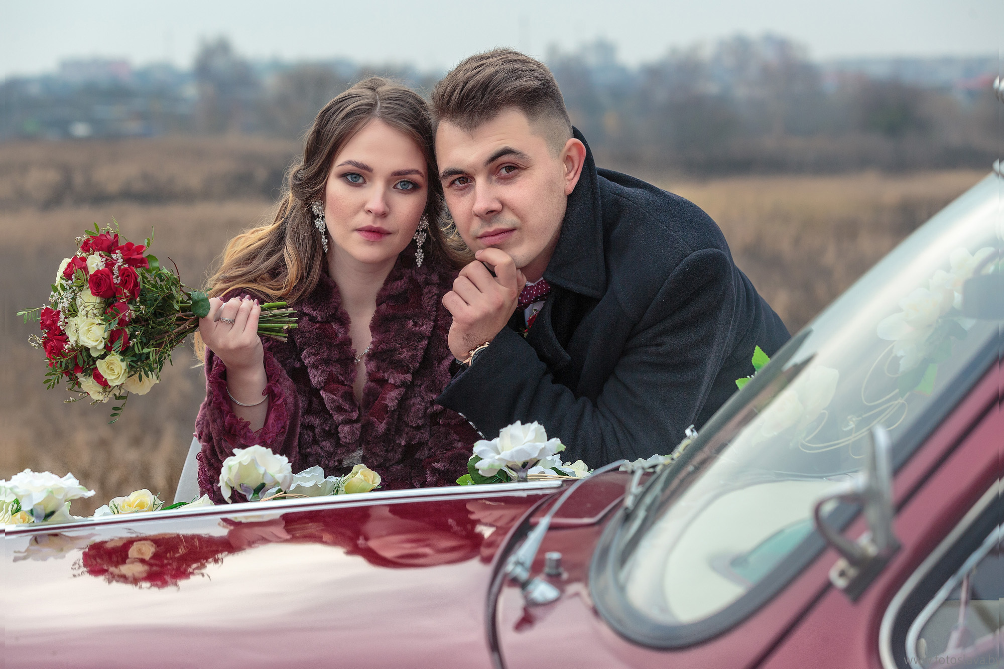 жених с невестой облокотились на капот автомобиля.