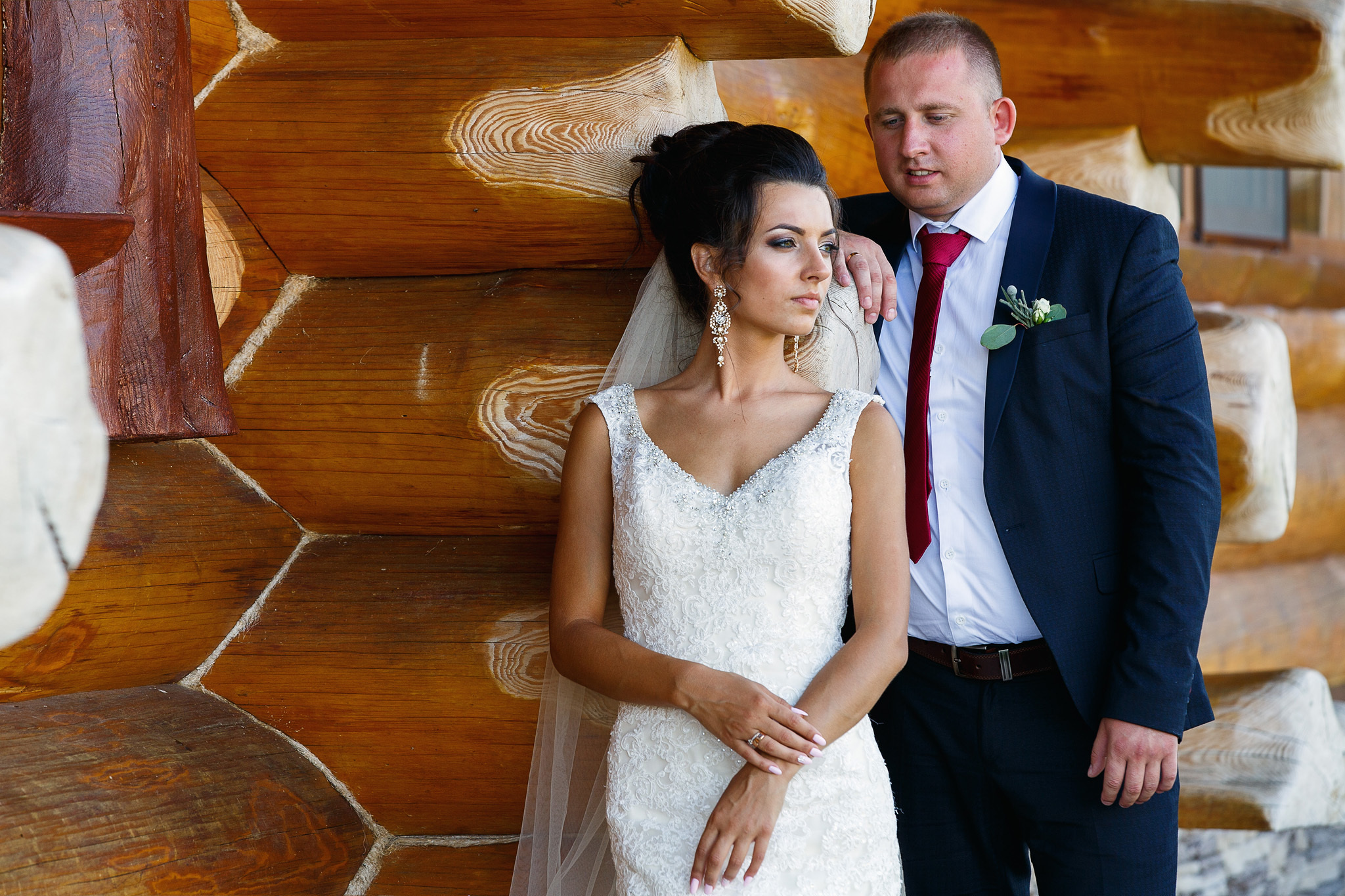 жених позади невесты на фоне деревянного дома.
