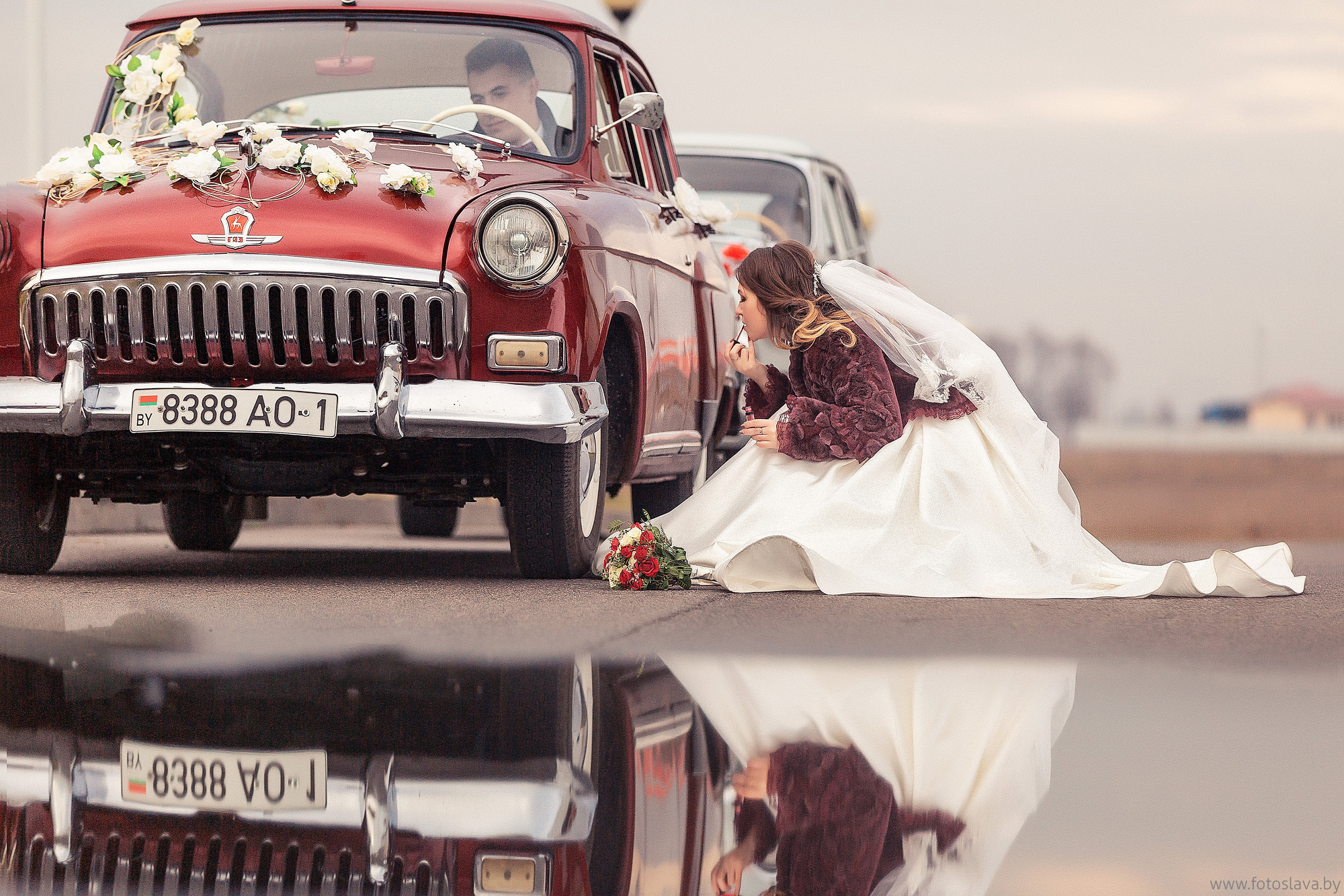 невеста смотрит в диск колеса ретро авто и красит губы.