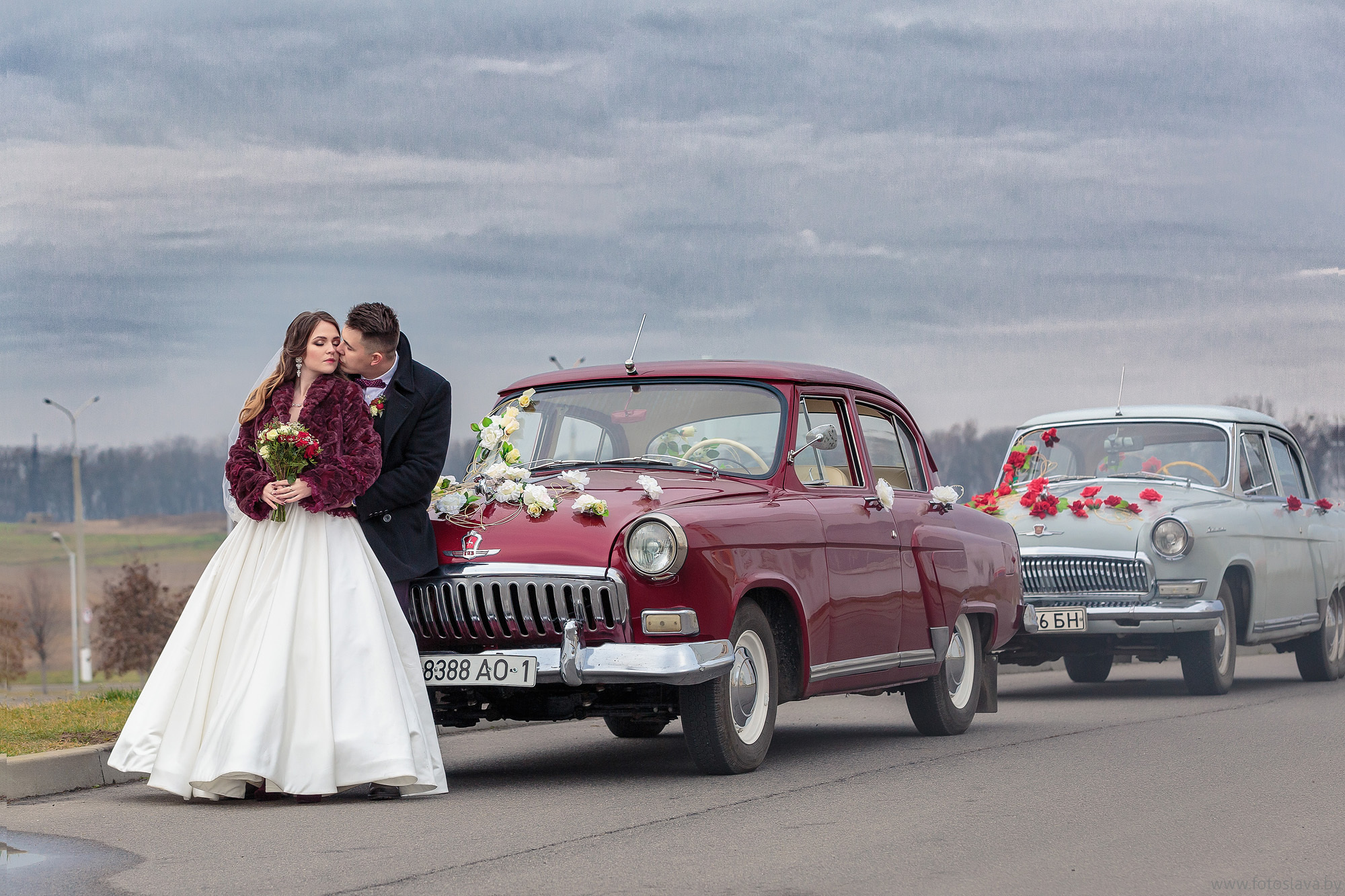 жених с невестой обнимаются перед машинами свадебного кортежа.