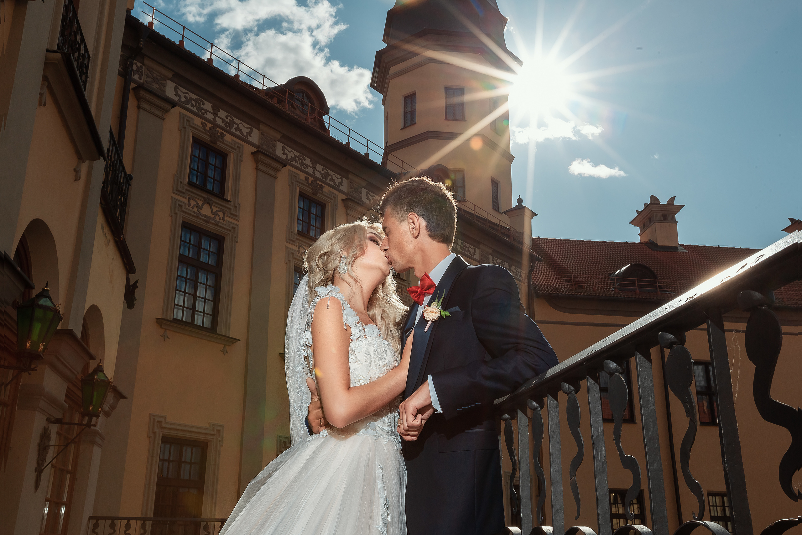 жених с невестой целуются на фоне синего неба в лучах солнца.