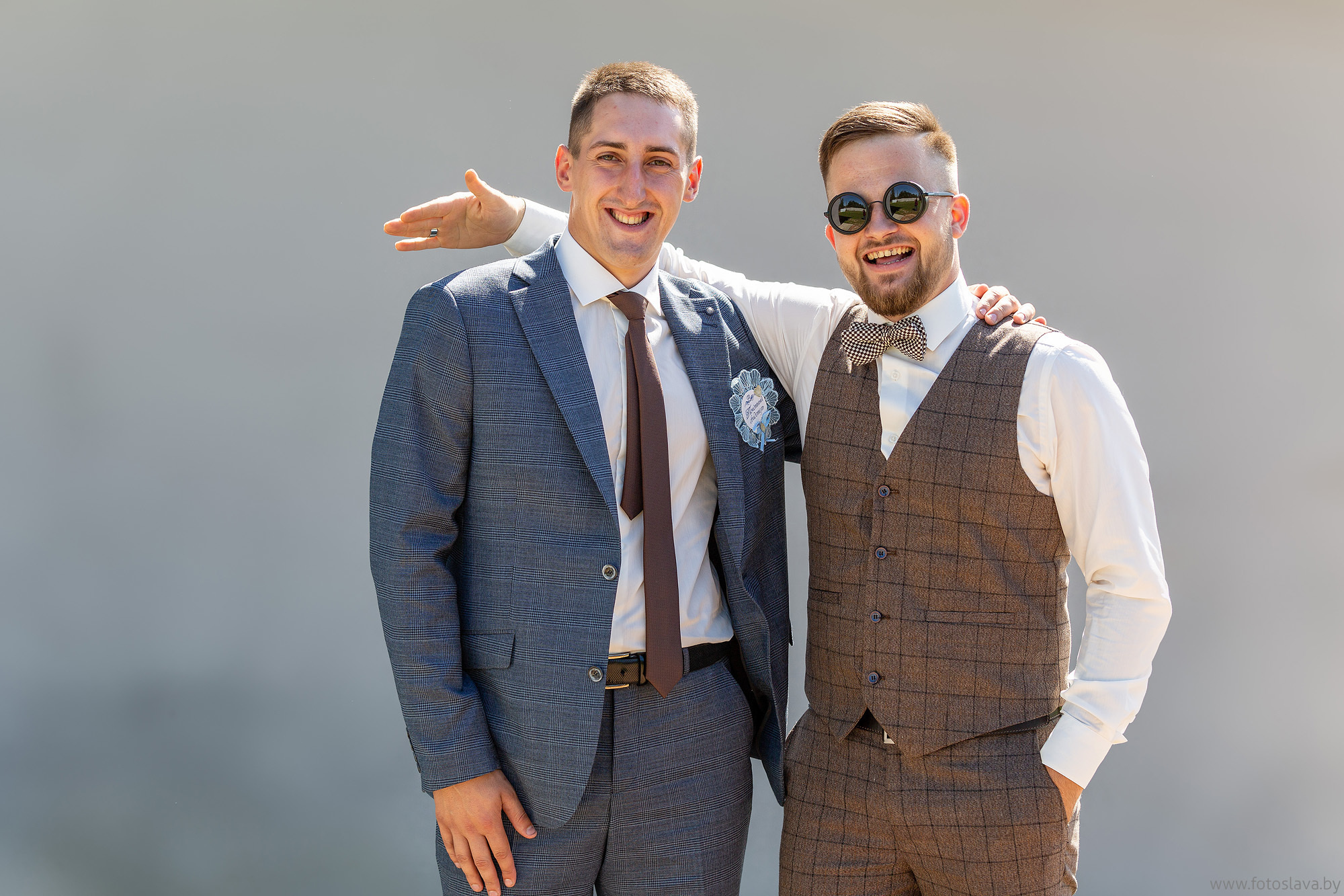 жених с другом в обнимку на ровном сероголубом фоне.