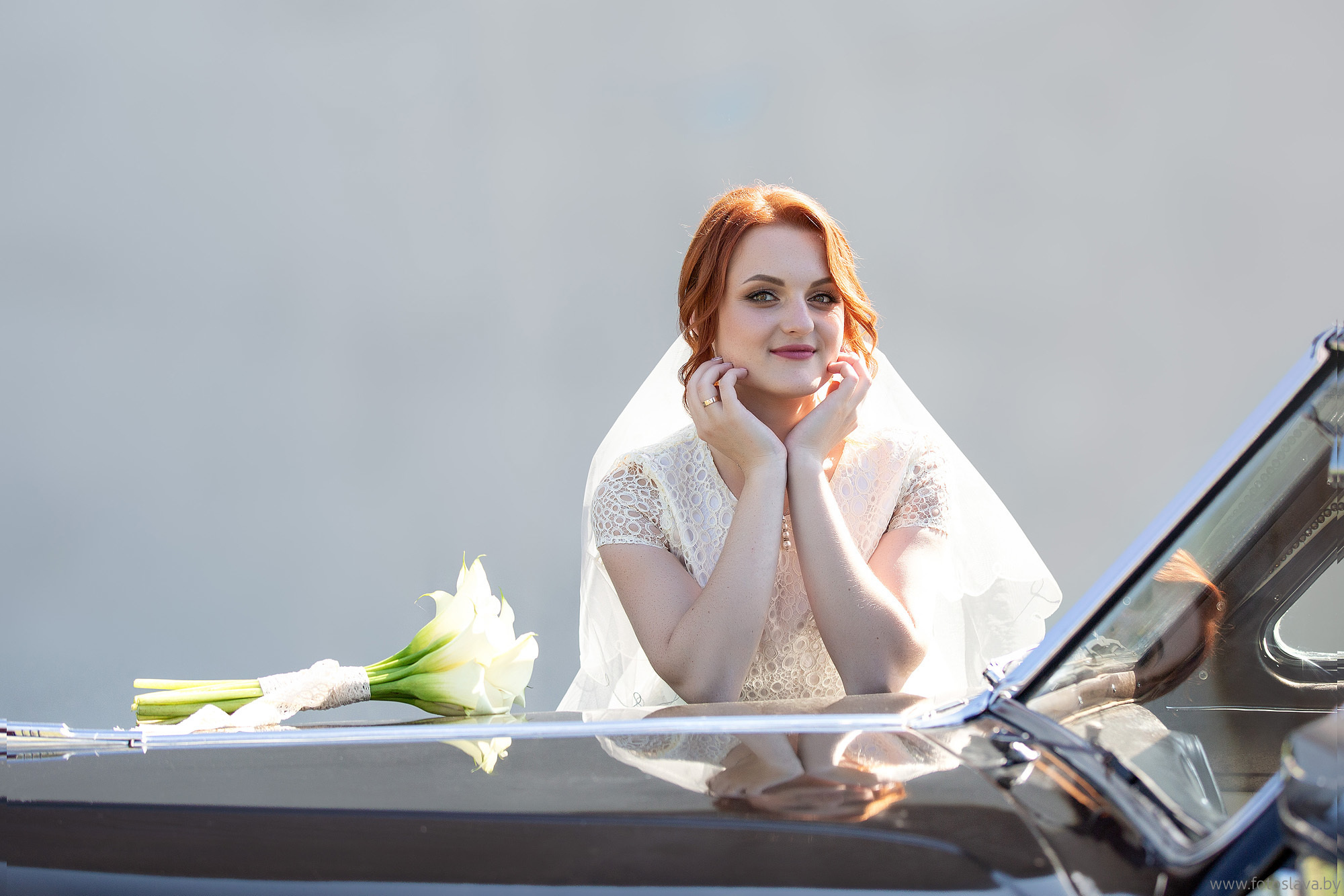 невеста локтем опирается на капот ретро автомобиля.