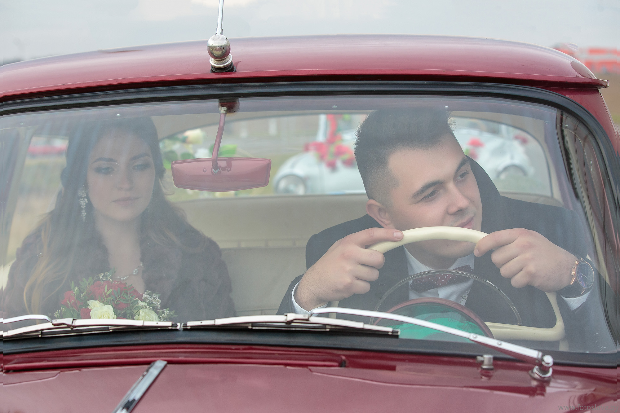 жених облокотился на руль, невеста на заднем сиденье , снято через стекло автомобиля.