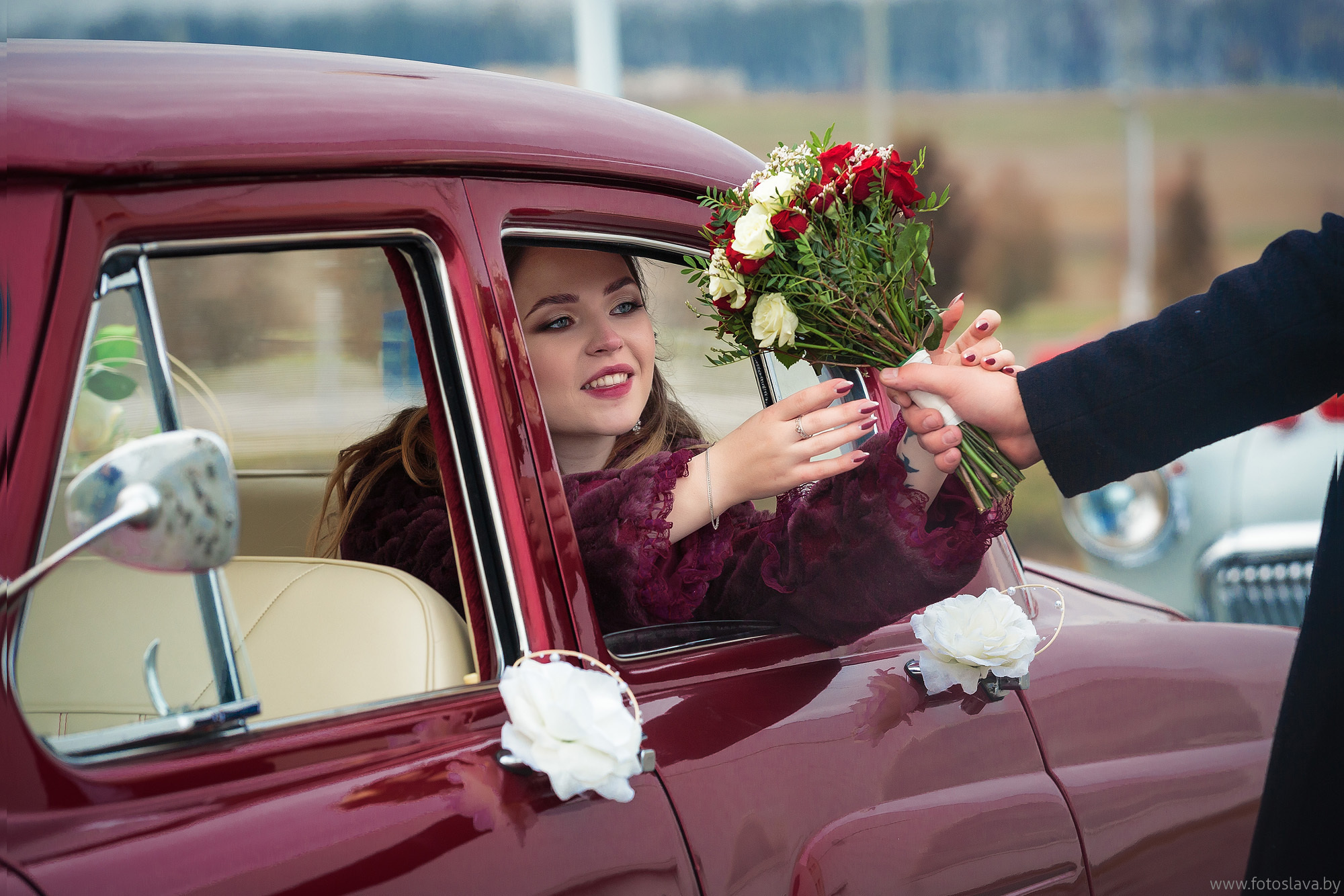 жених подает букет невесте сидящей в машине.