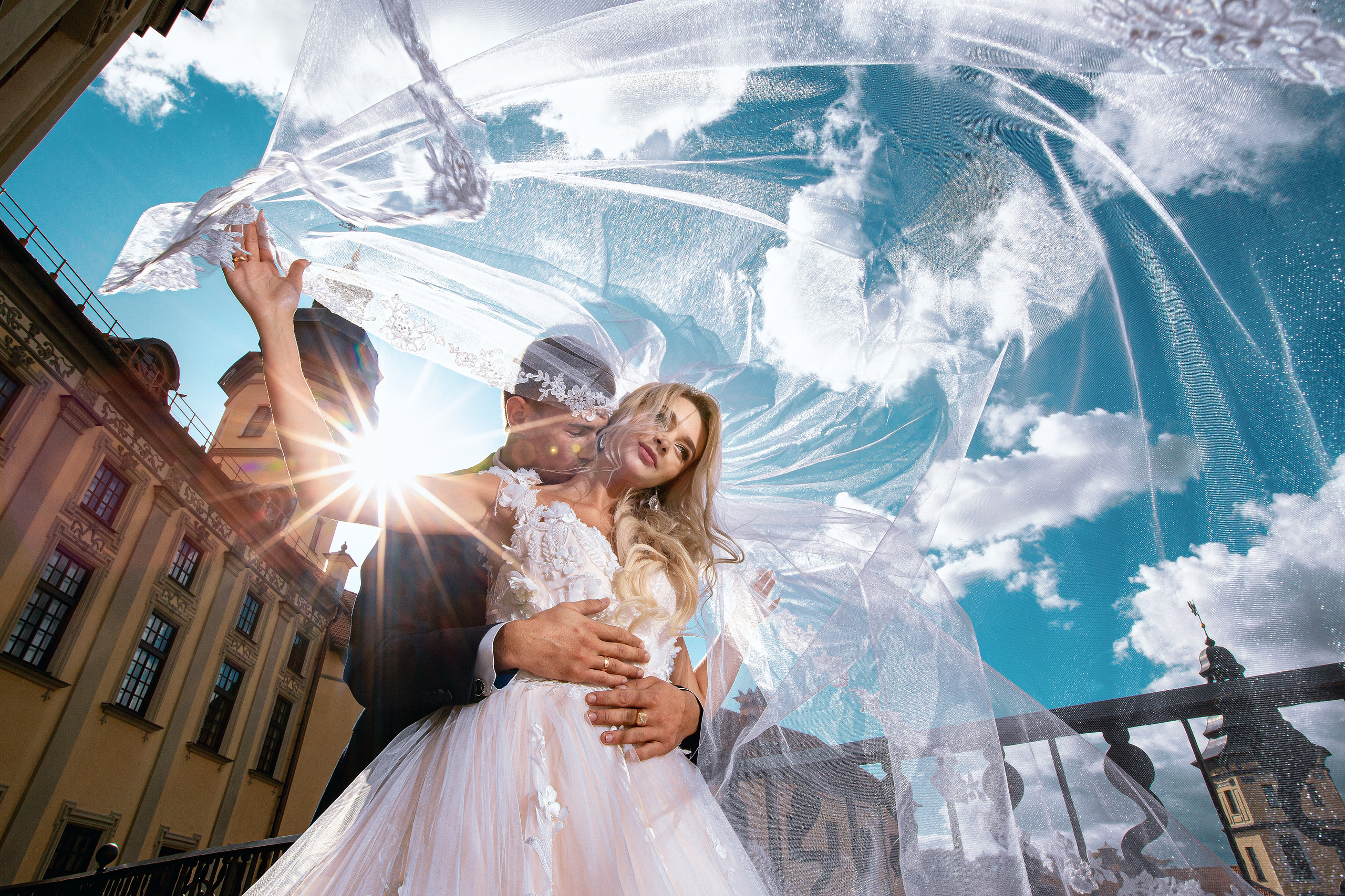 жених сзади обнимает невесту на фоне развевающейся фаты.