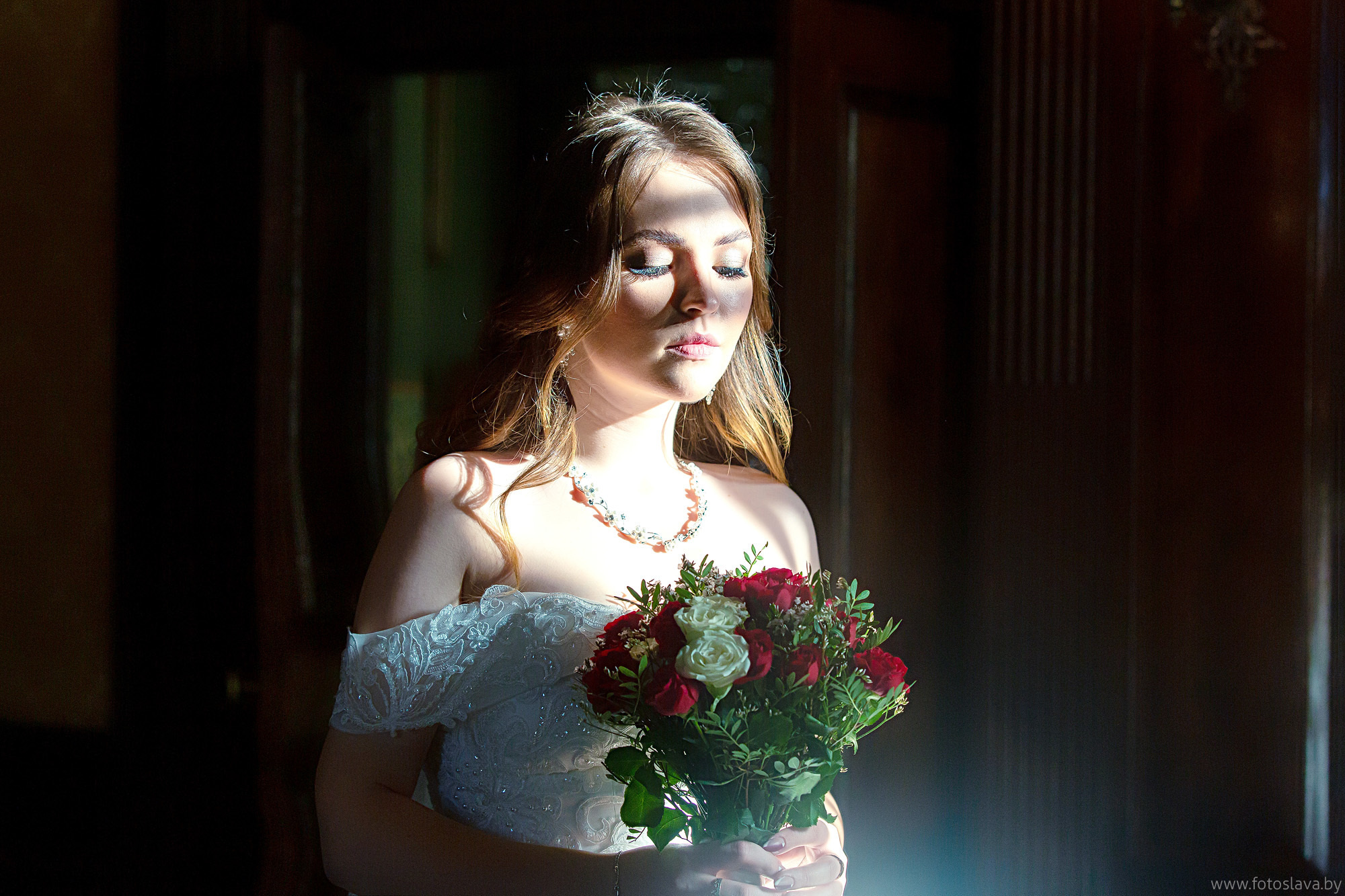 невеста с букетом у окна в лучах солнца на темном фоне.