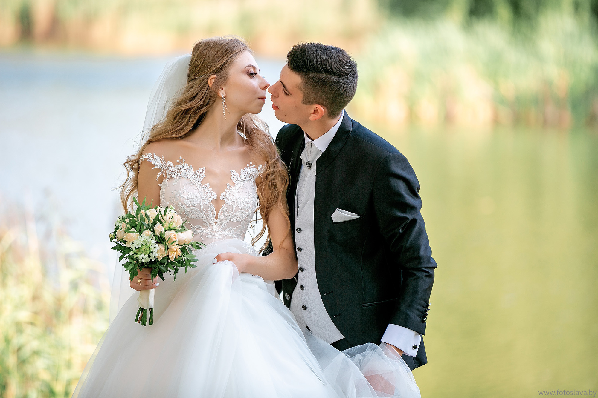 красиво целуются молодожены на зеленом фоне.