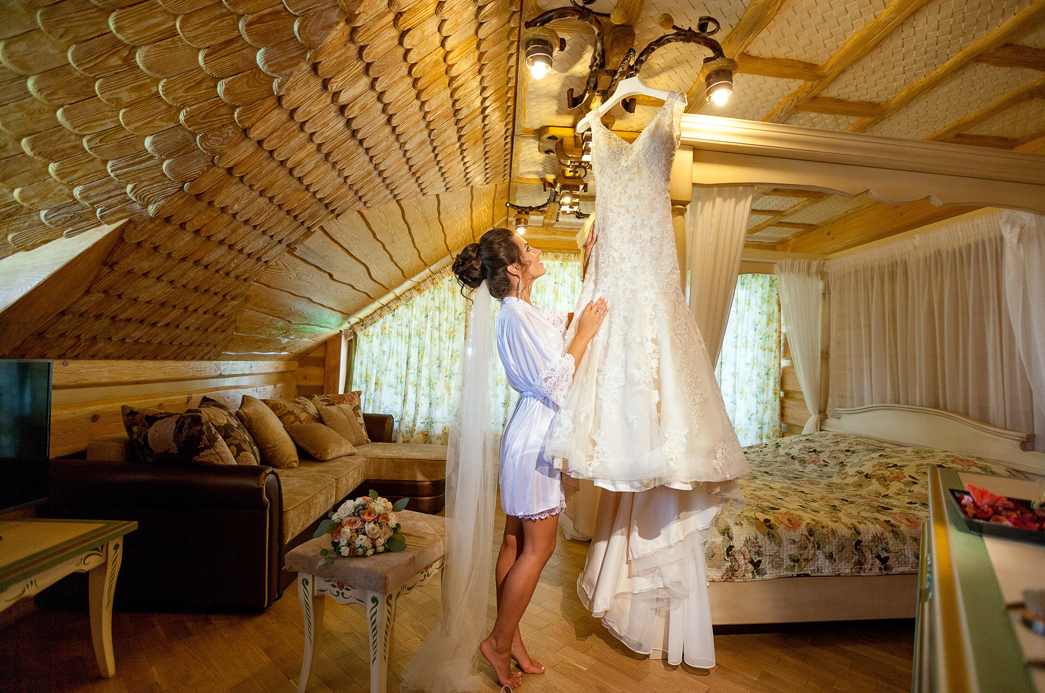 невеста в пеньюаре любуется свадебным платьем.