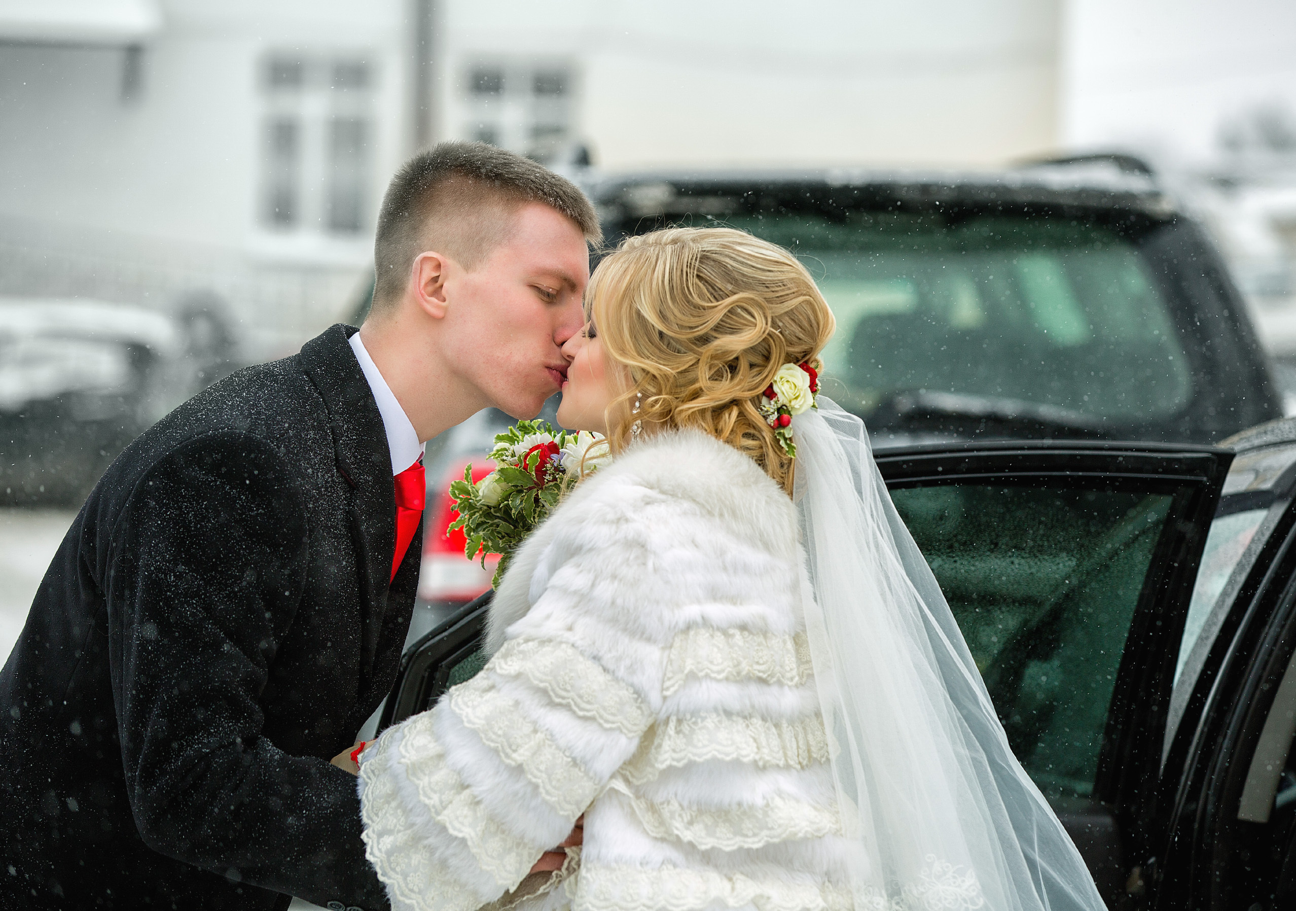 жених и невеста целуются у машины.