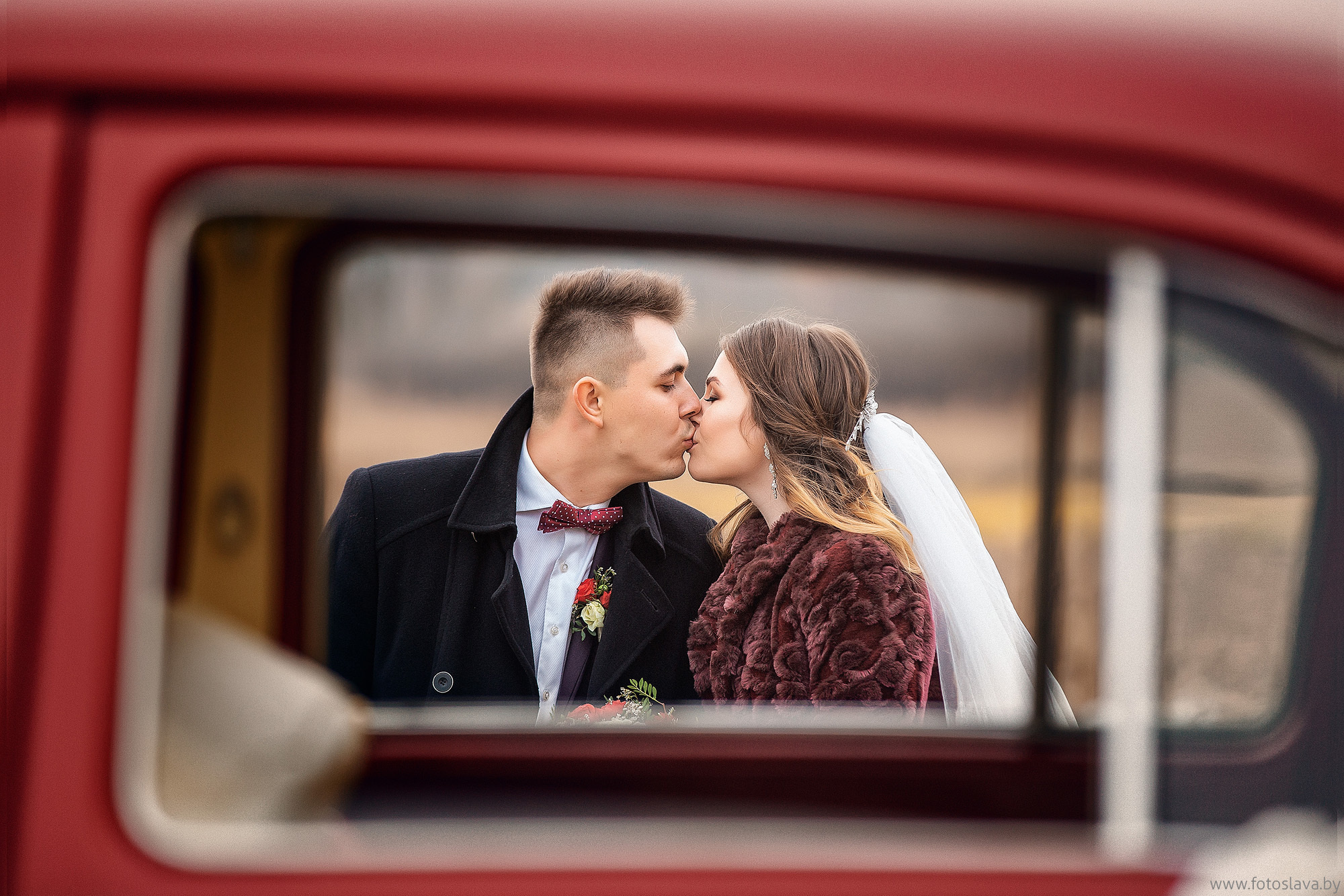 молодые на улице целуются в рамке окна автомобиля.