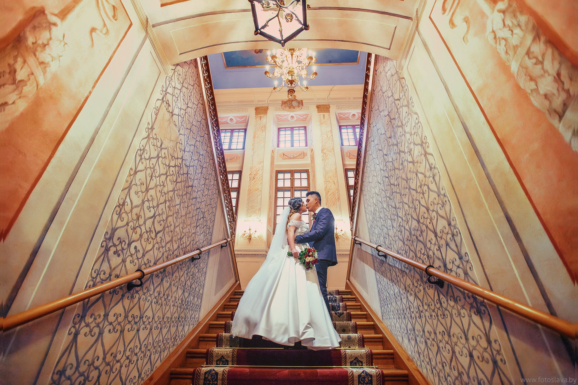 жених с невестой в полный рост на красивой лестнице в замке.