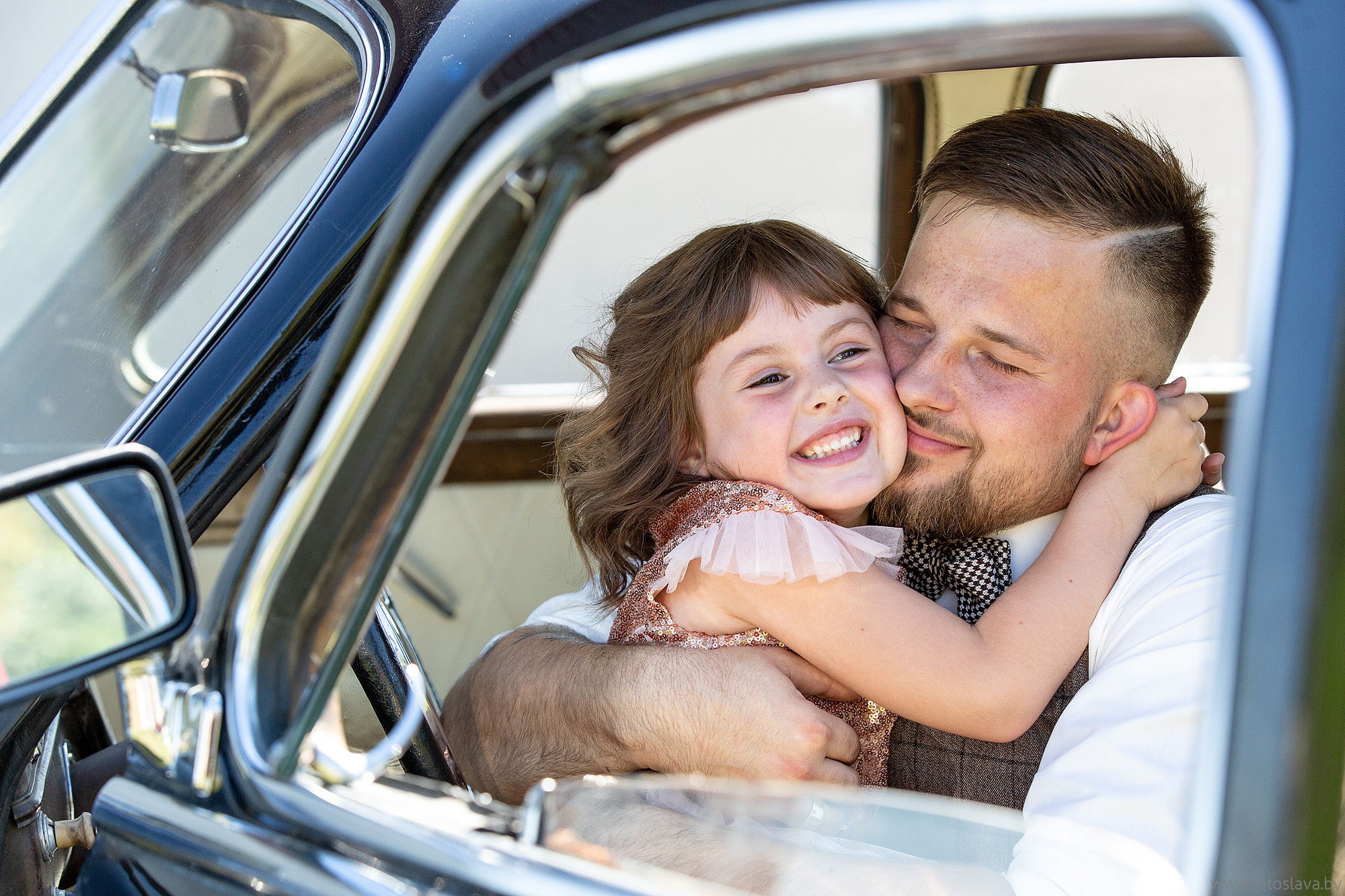жених сидит в машине и обнимает ребенка.