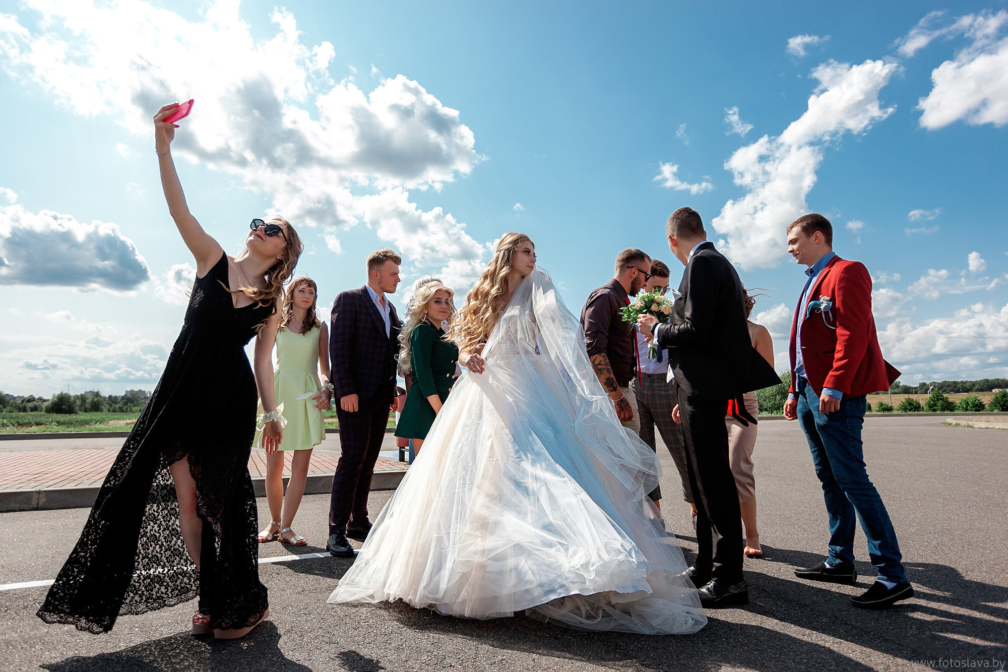 невеста и жених в окружении друзей веселятся на фоне синего неба.