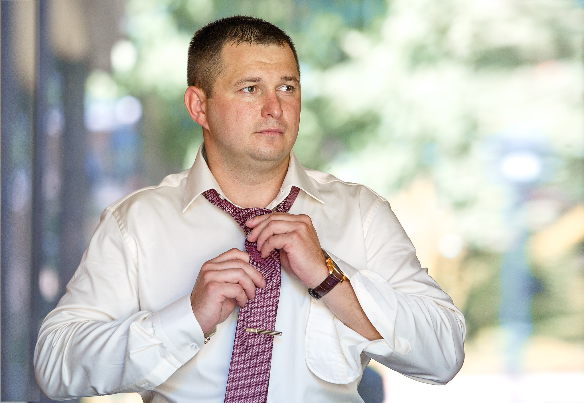 жених в белой рубашке застегивает галстук на улице.