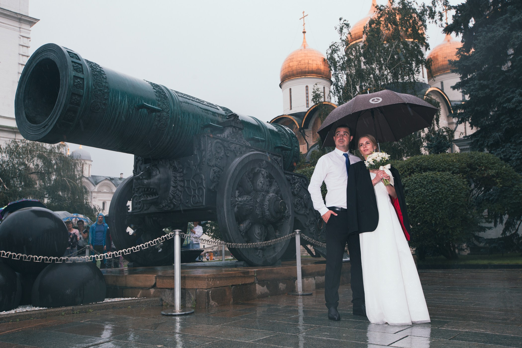 свадебная фотосьемка где невеста с женихом стоят у памятника с зонтом 