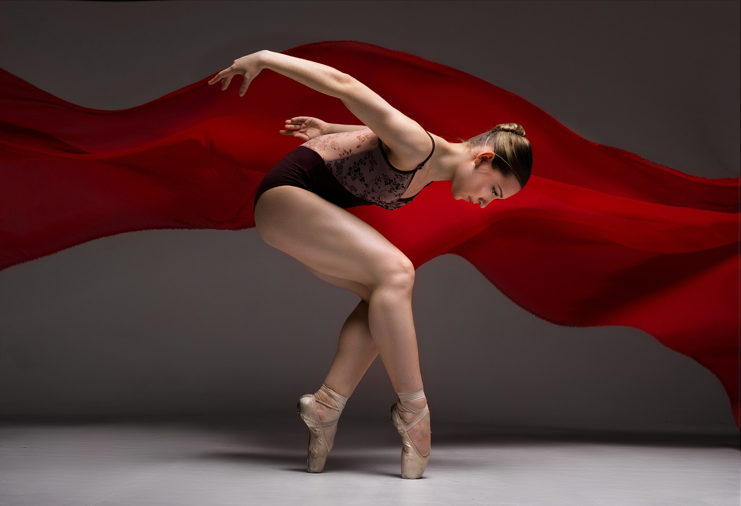 Экспрессивный кадр с балериной и летящей красной тканью. Акцент на динамике движения, силе и эстетике балета на фоне красной ткани.