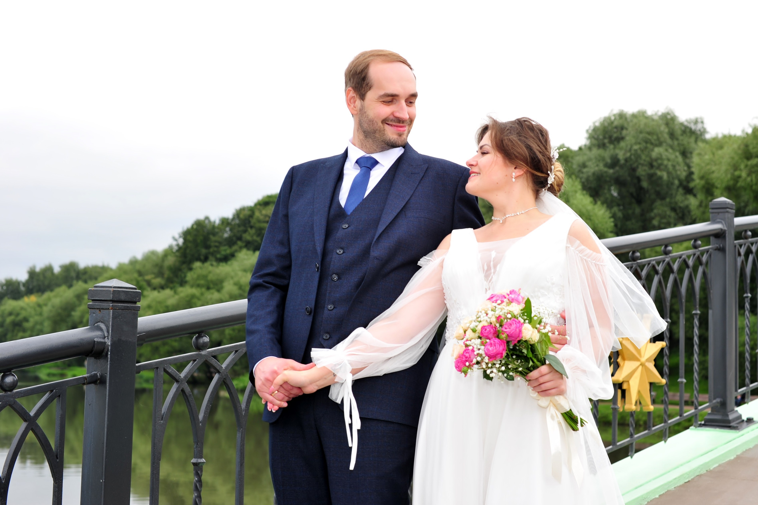 Свадьба в Царицыно пасмурным летним днем, молодожены идут по металлическому мосту и держатся за руки 