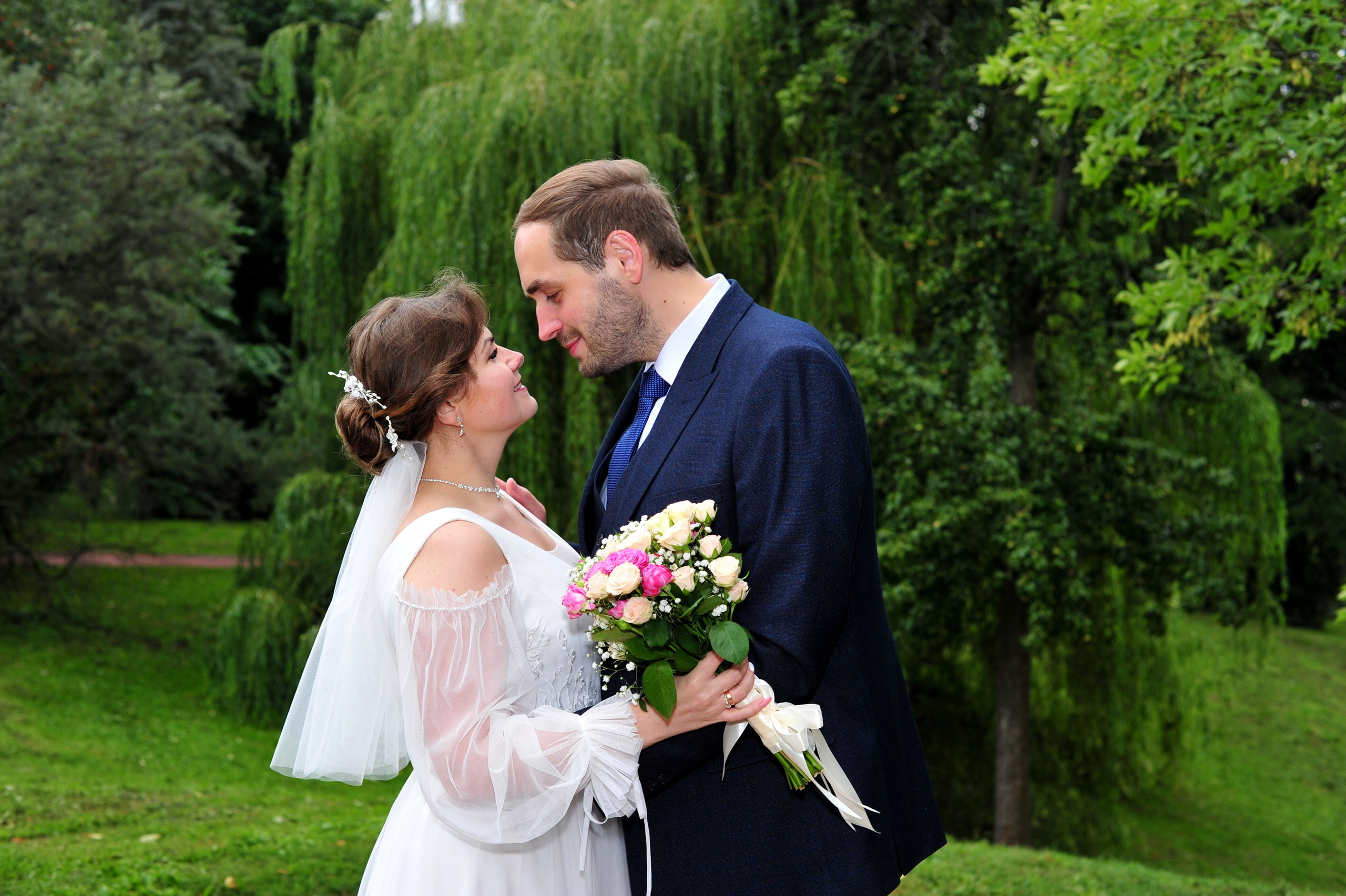 Свадьба в Царицыно пасмурным летним днем, молодожены смотрят друг на друга на фоне изумрудной зелени в парке 