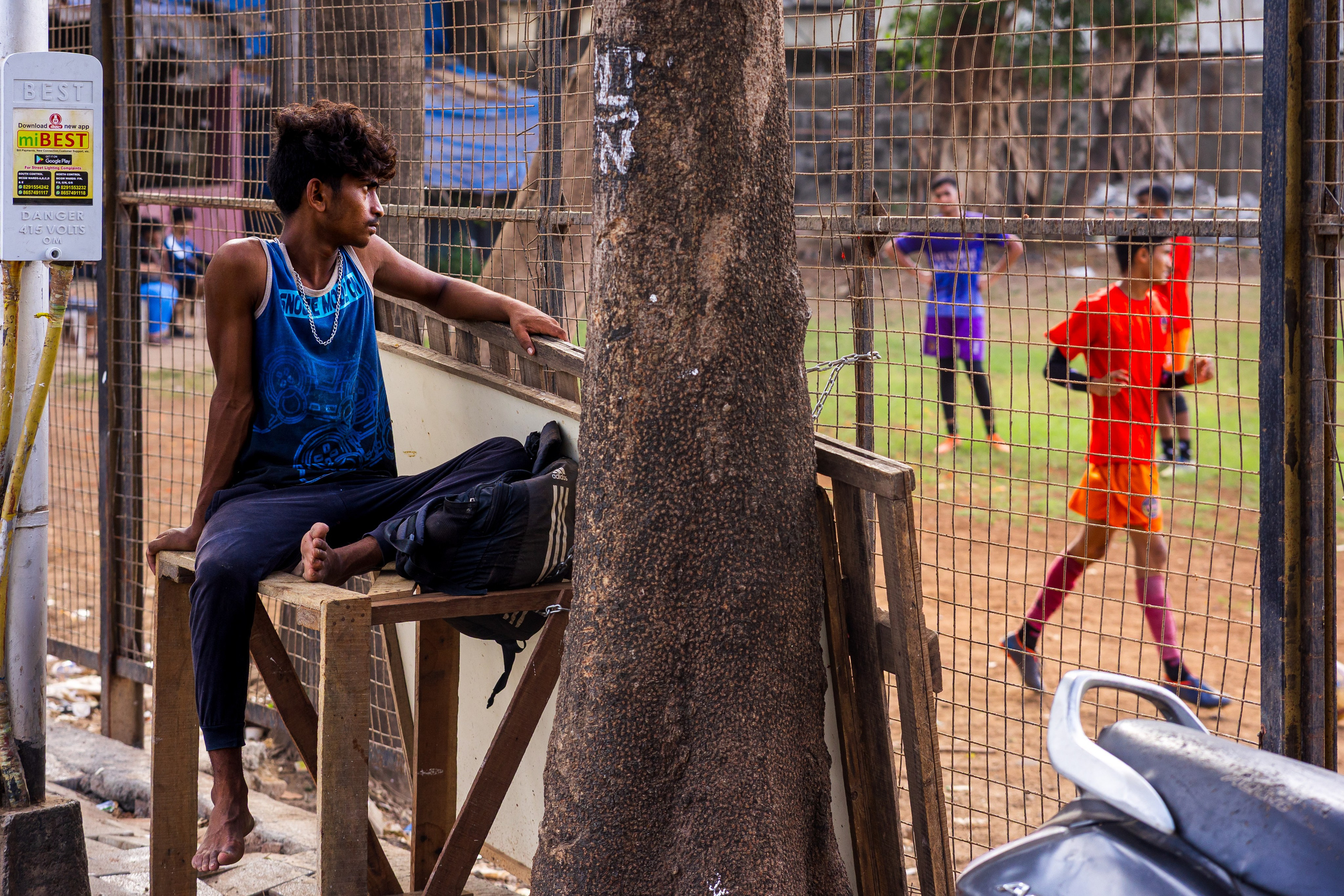 Мальчик в синей футболке сидит на возвышении, дети играют на площадке