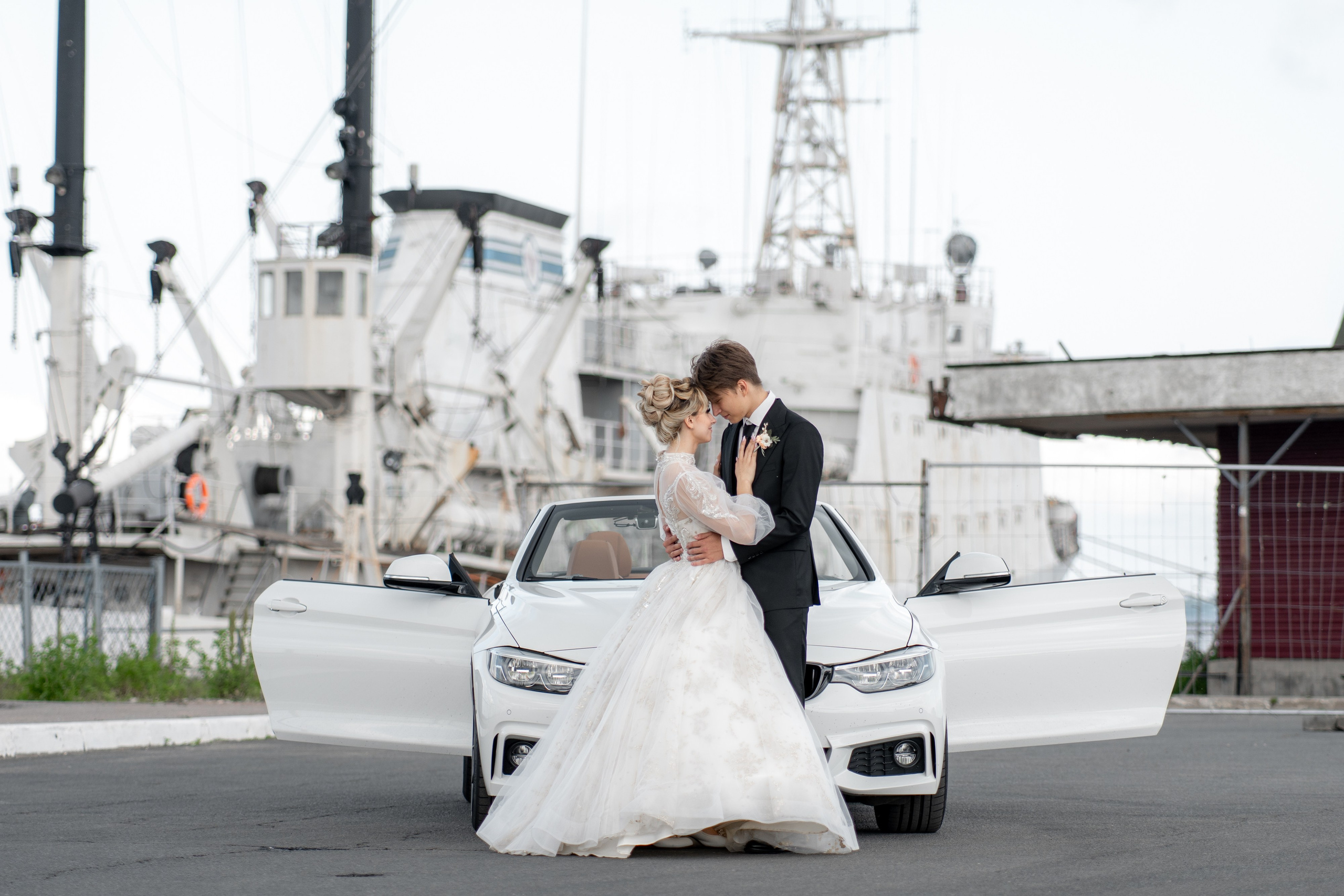 Свадебная фотосессия на пристани в Ломоносове на белом кабриолете. Жених и невеста обнимаются на фоне машины