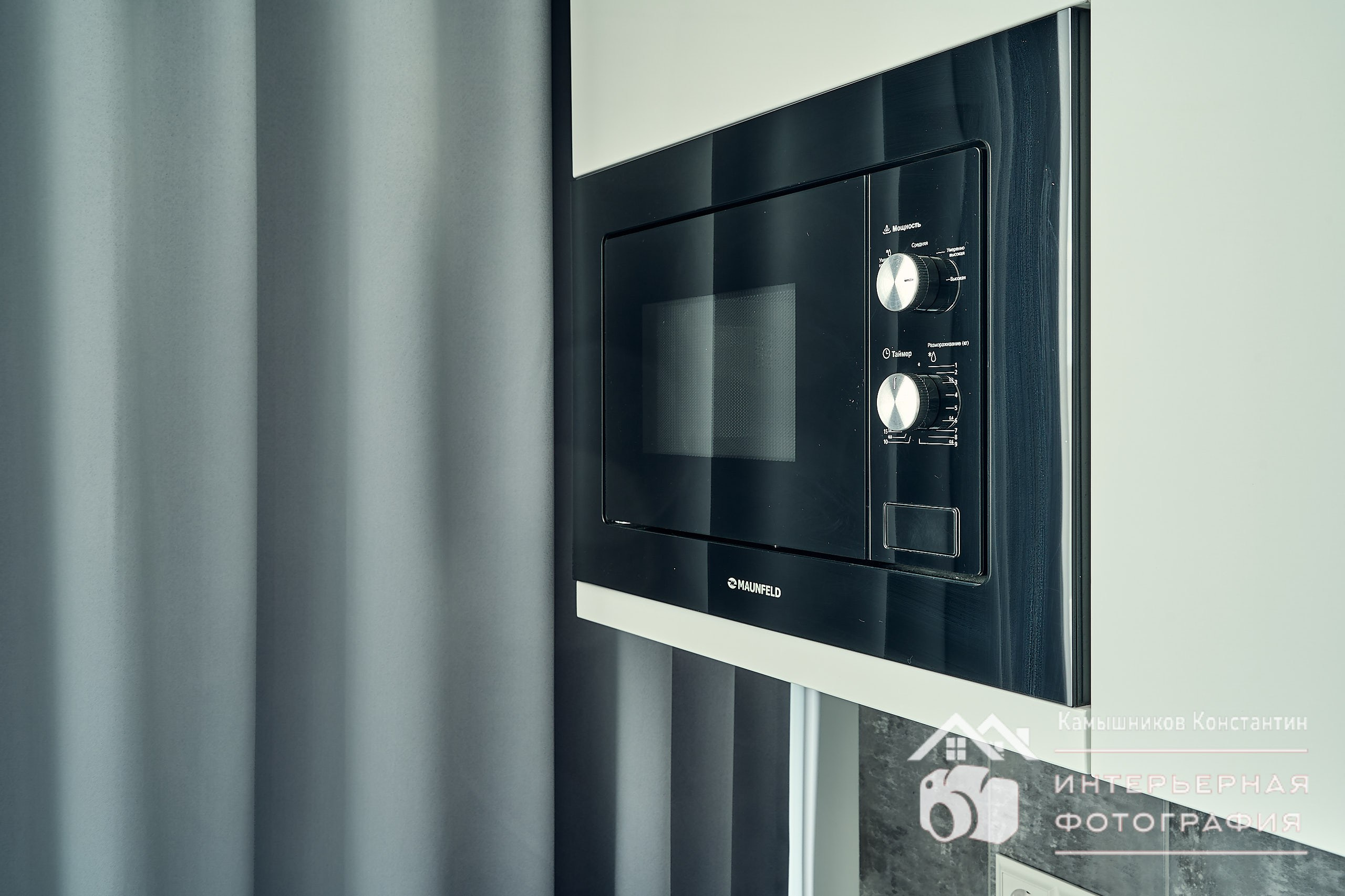 Интерьерная фотография крупного плана микроволновки на кухне в квартире в ЖК бизнес-класса на мягком фоне складок штор