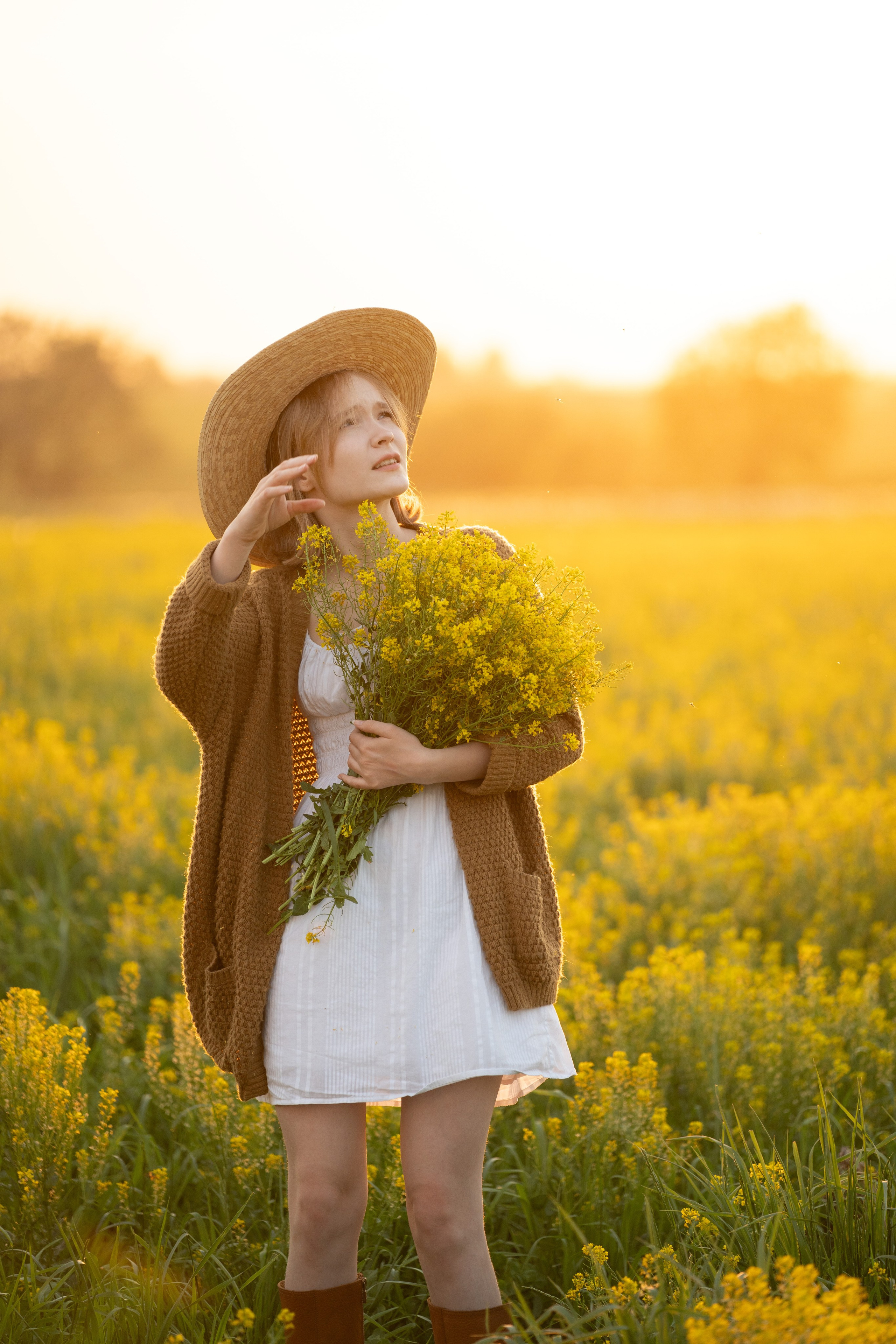 Портрет подростка или девушки на природе в поле. Она смотрит в небо. Девочка одета в легкое платье и поверх накинута кофта. Букет полевых цветов держит в руках.