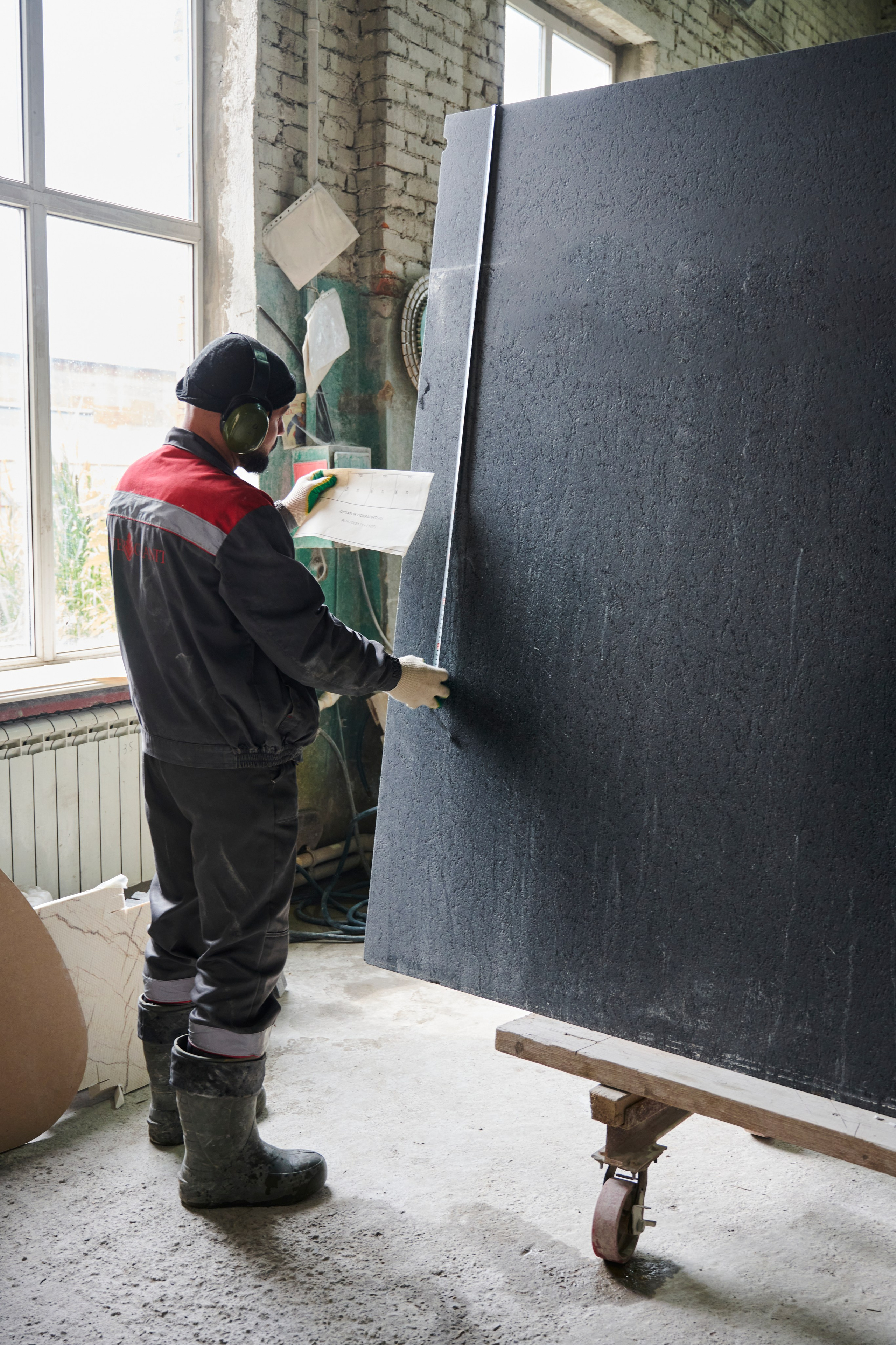 Большой чёрный слэб вертикально, рабочий проверяет поверхность