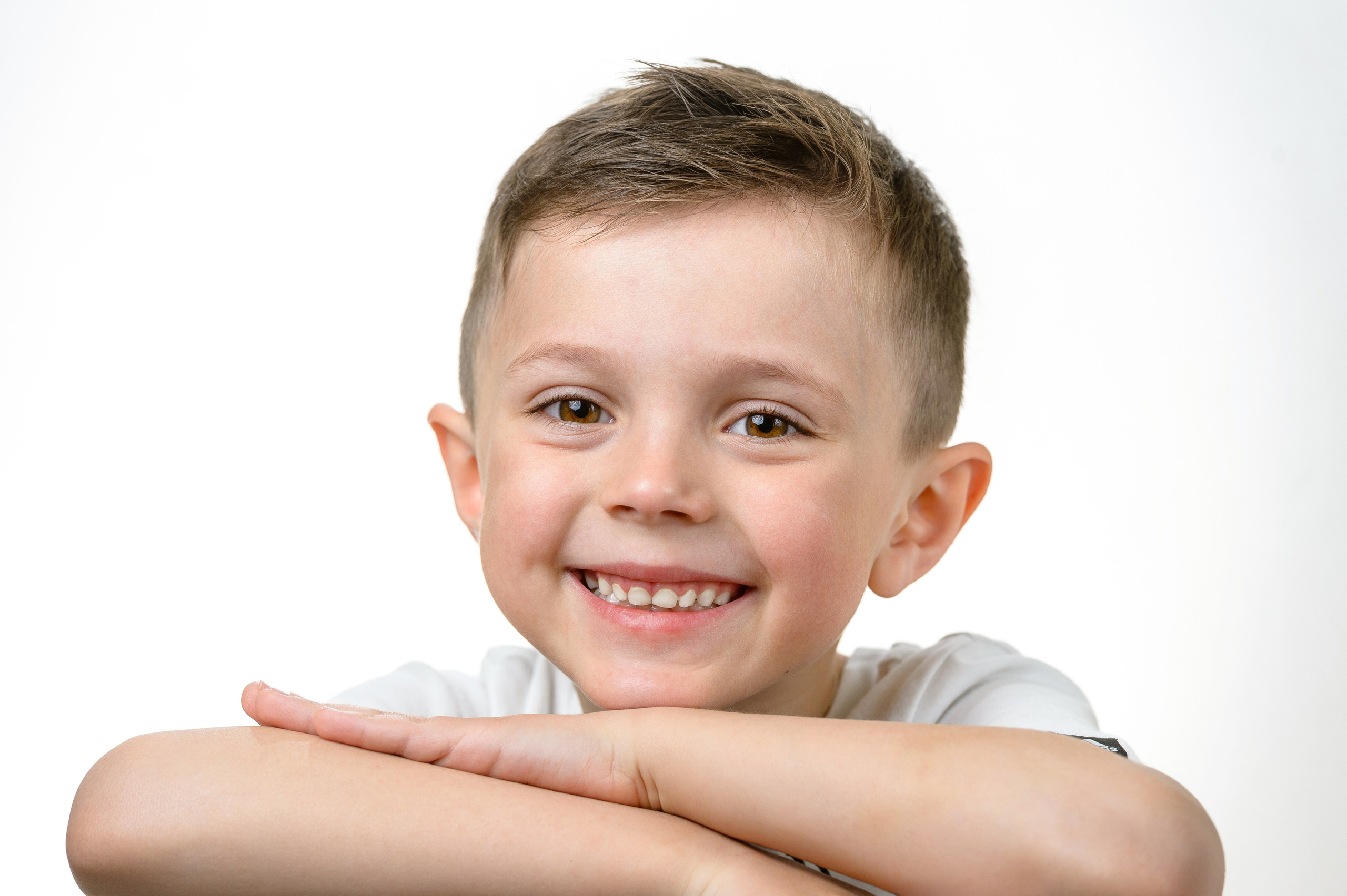 Портрет мальчика: лежит, положив руки под подбородок, и смотрит в камеру на светлом фоне.