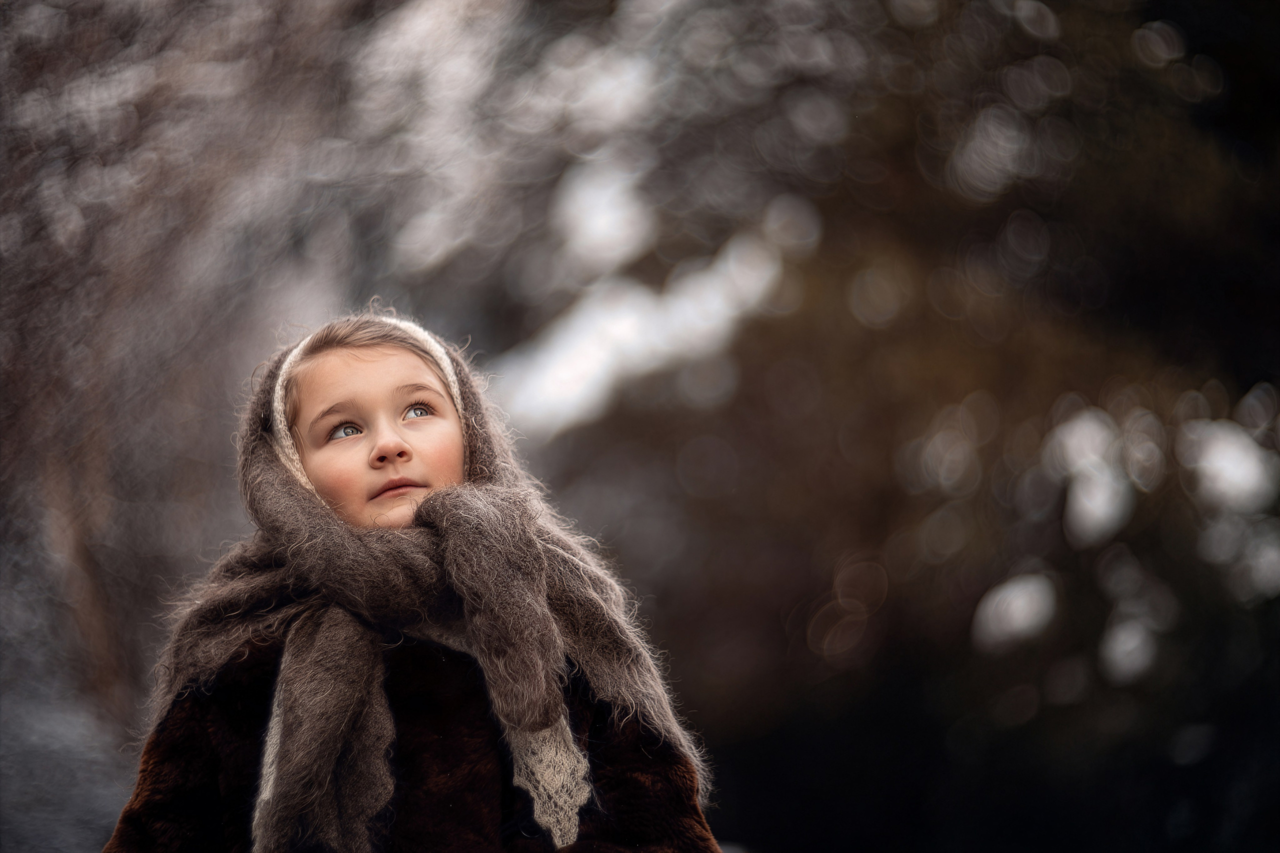 Девочка в шерстяном платке смотрит вверх на фоне зимнего леса — детская фотосессия в Подмосковье