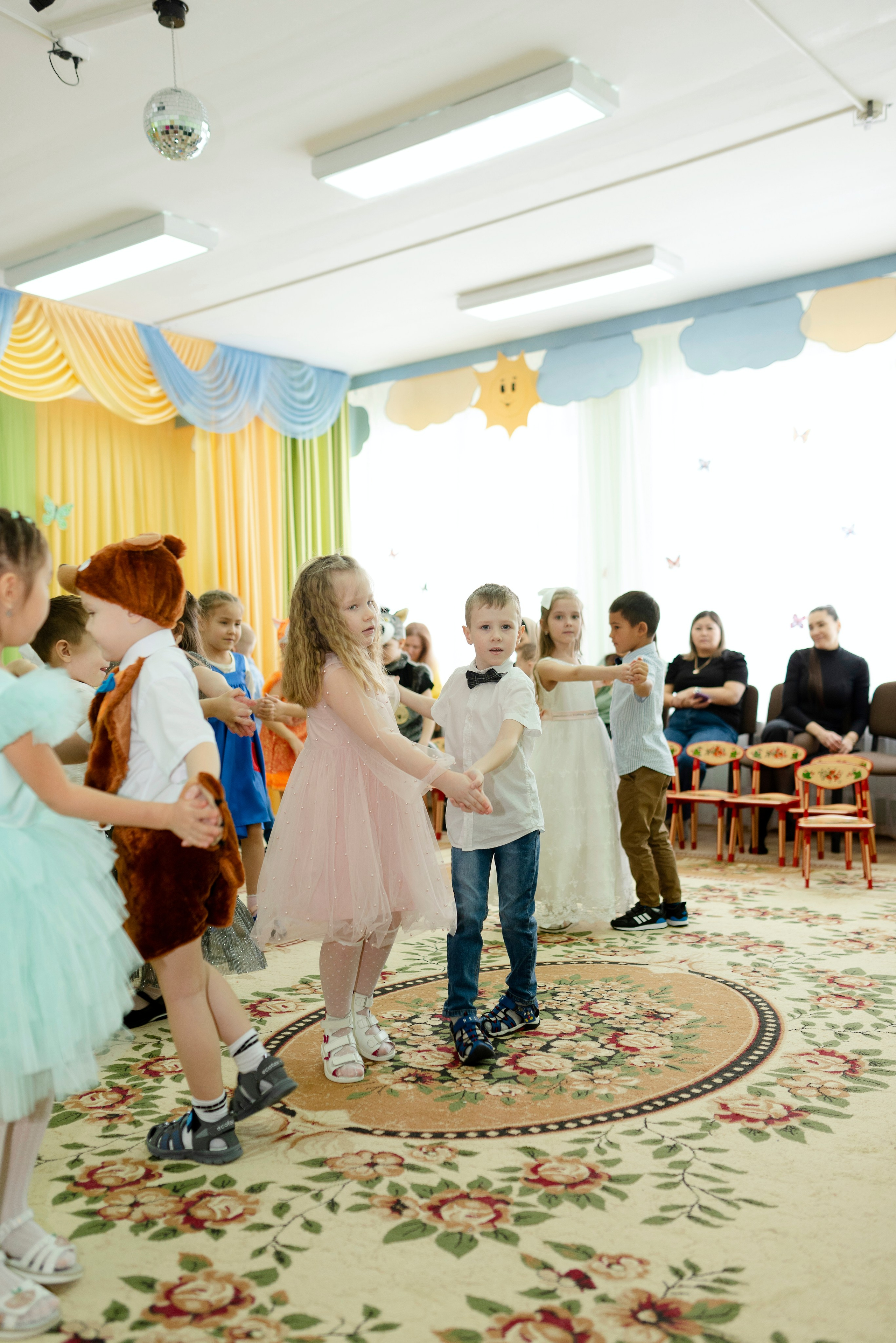 Дети танцуют веселый танец в праздничных костюмах на утреннике 8 марта в детском саду.