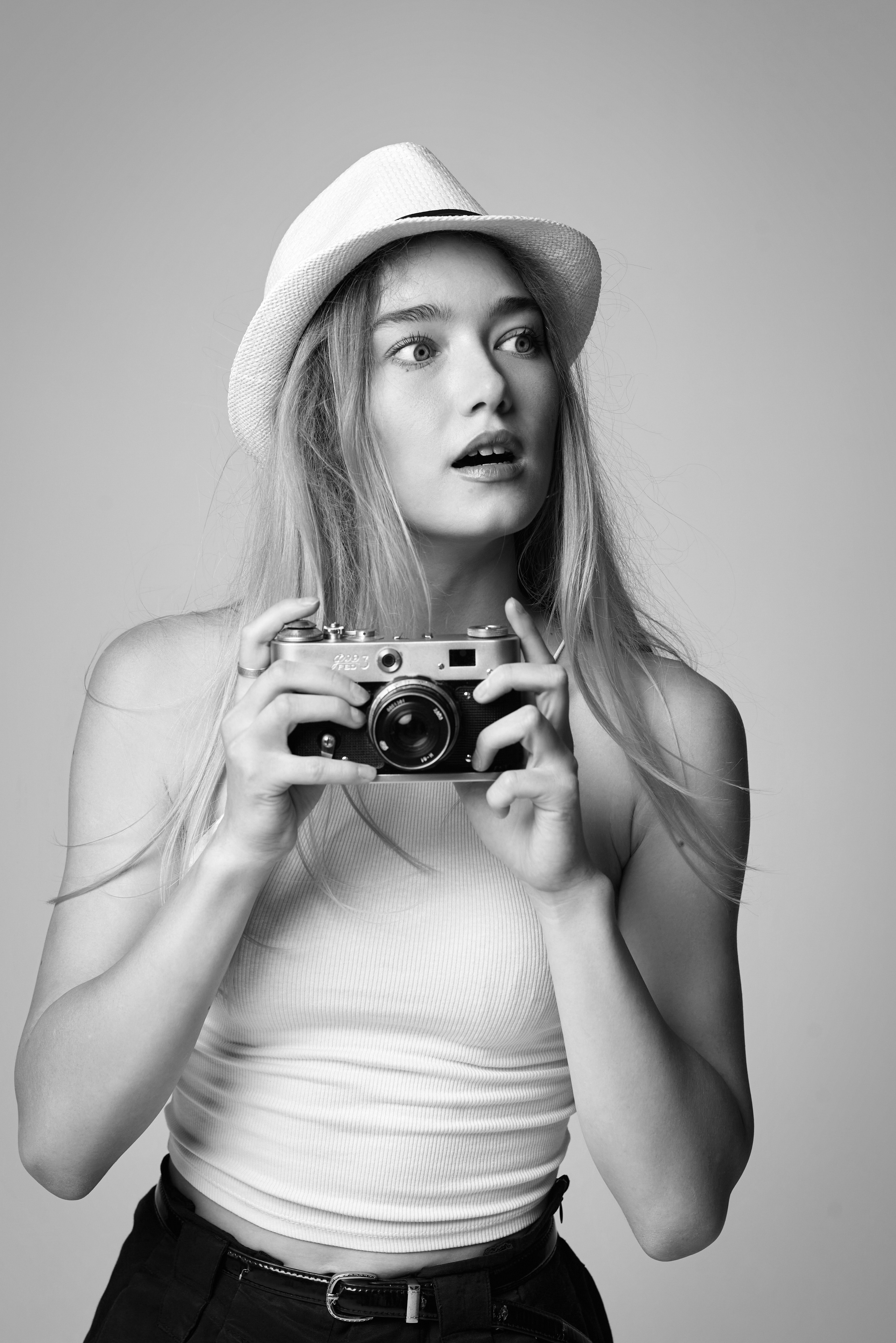 Фото светловолосой модели Алисы в студии на светлом фоне в черном платье с вырезом на спине.