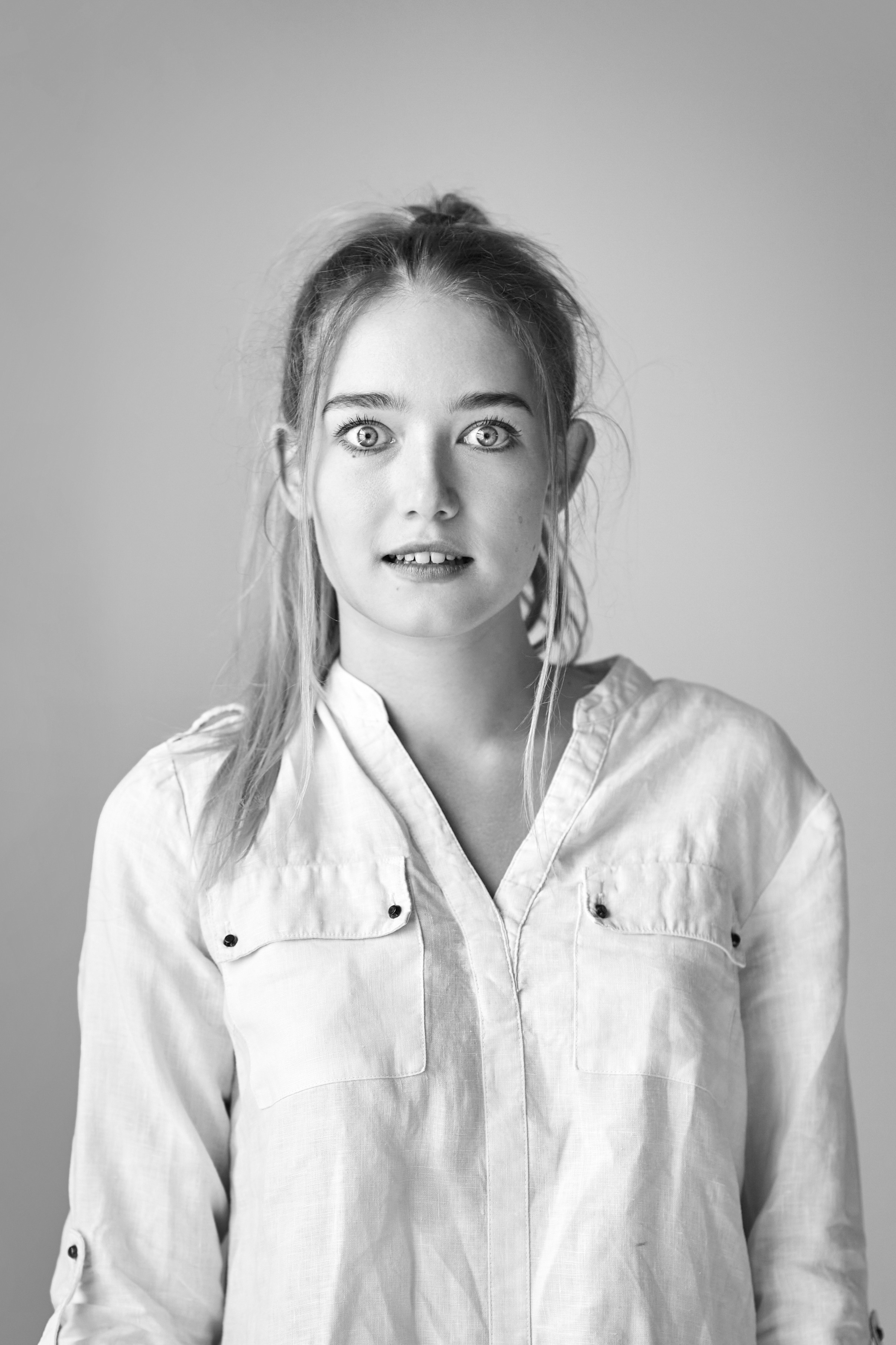 Красивая светловолосая модель Алиса позирует в студии на светлом фоне, одетая в платье или рубашку.