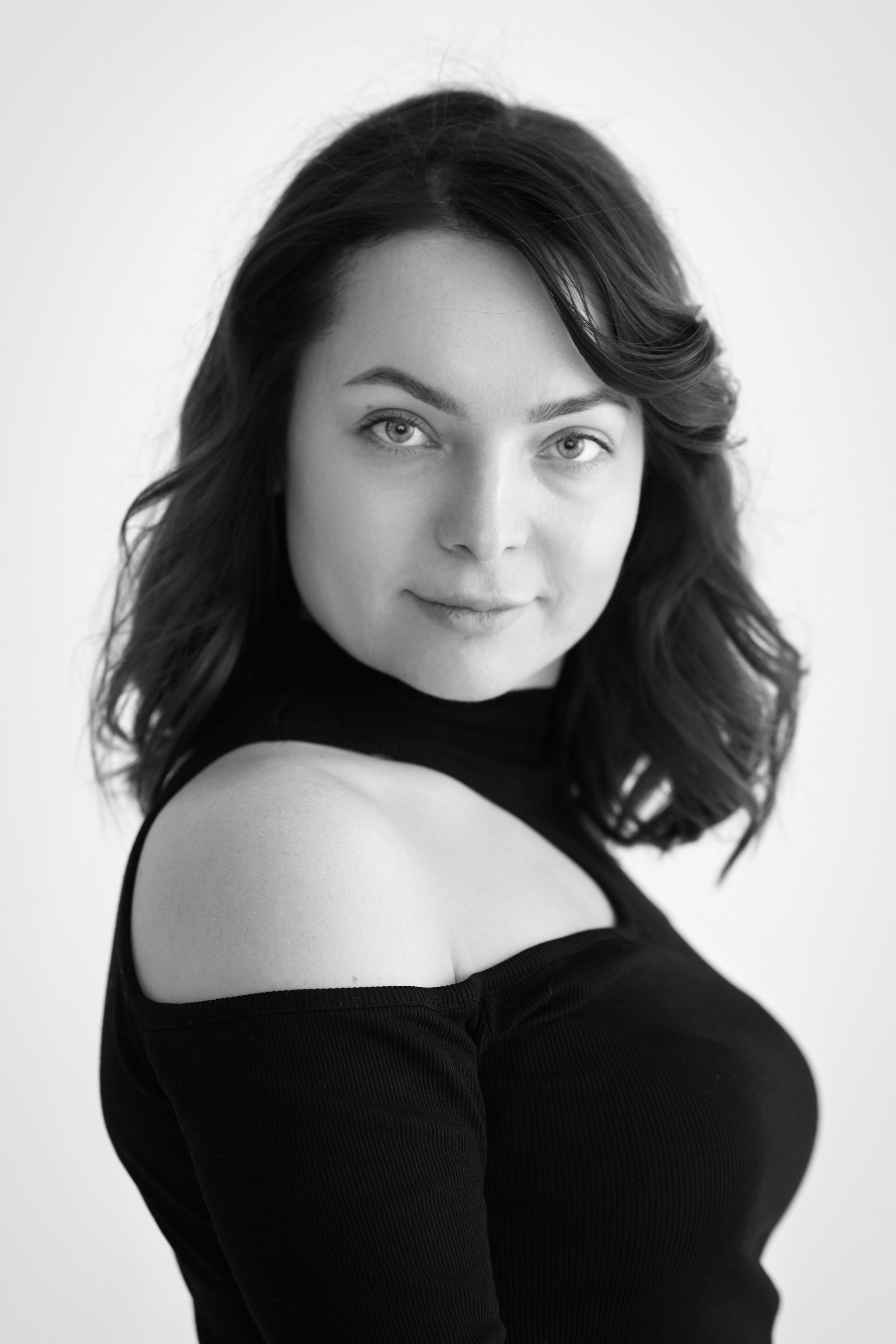 Темноволосая модель Татьяна сидит на стуле в светлой рубашке на светлом фоне в студии.